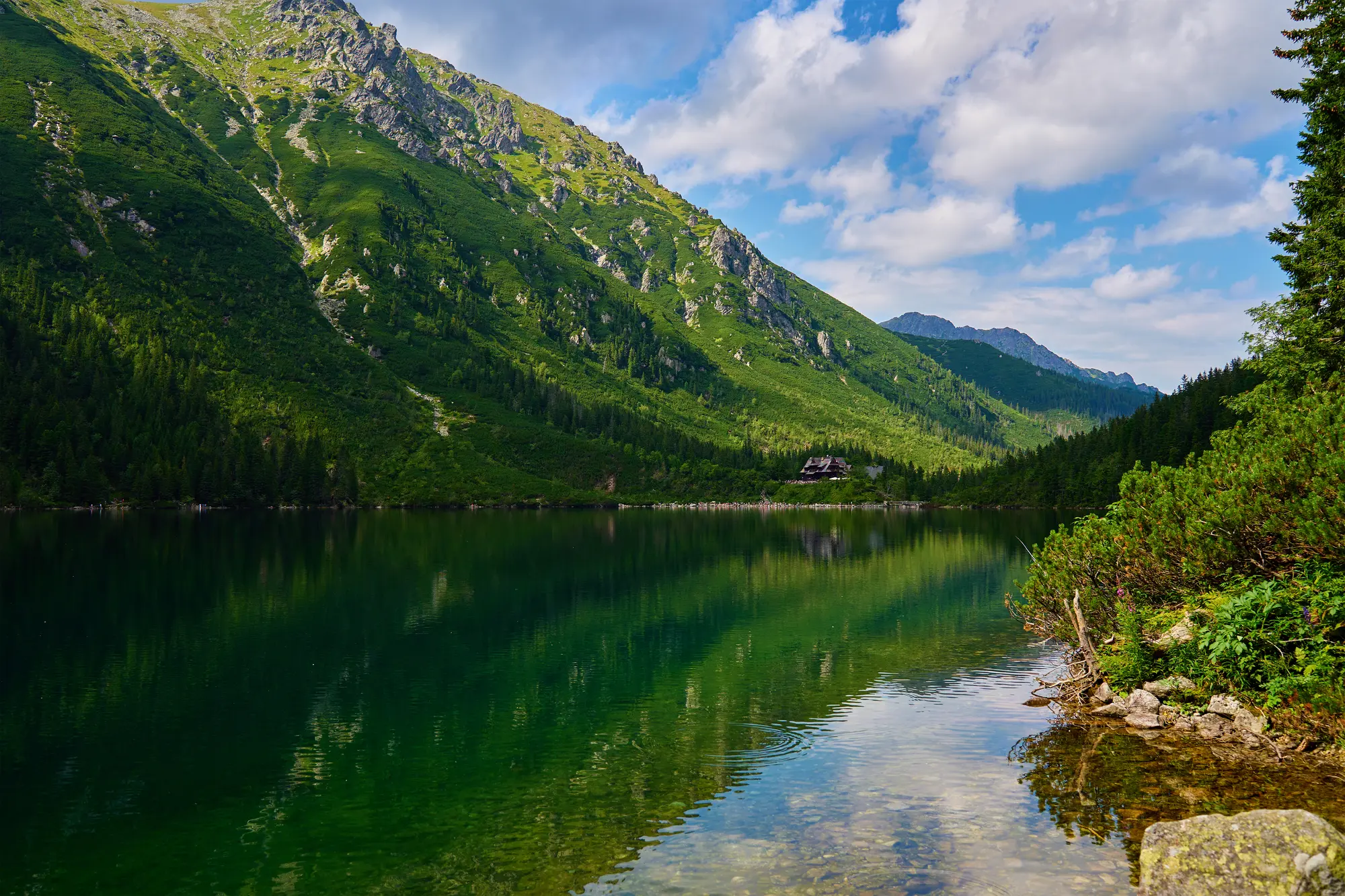 Green mountains reflecting in a calm green Morskie Oko Lake on a sunny day in the Tatra Mountains Zakopane.