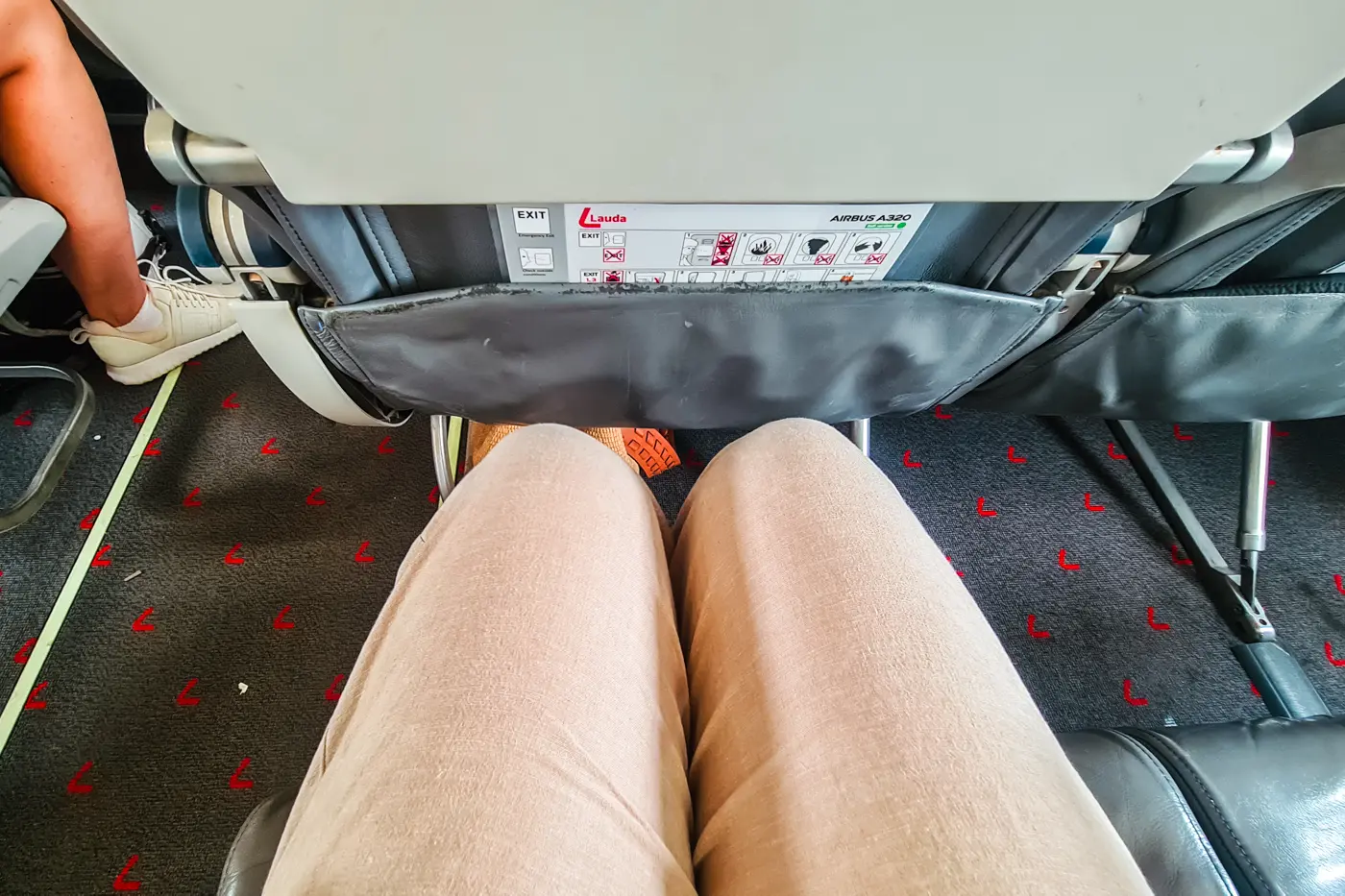 View from above of legs with beige pants sitting in a seat showing the legroom in a Ryanair plane.