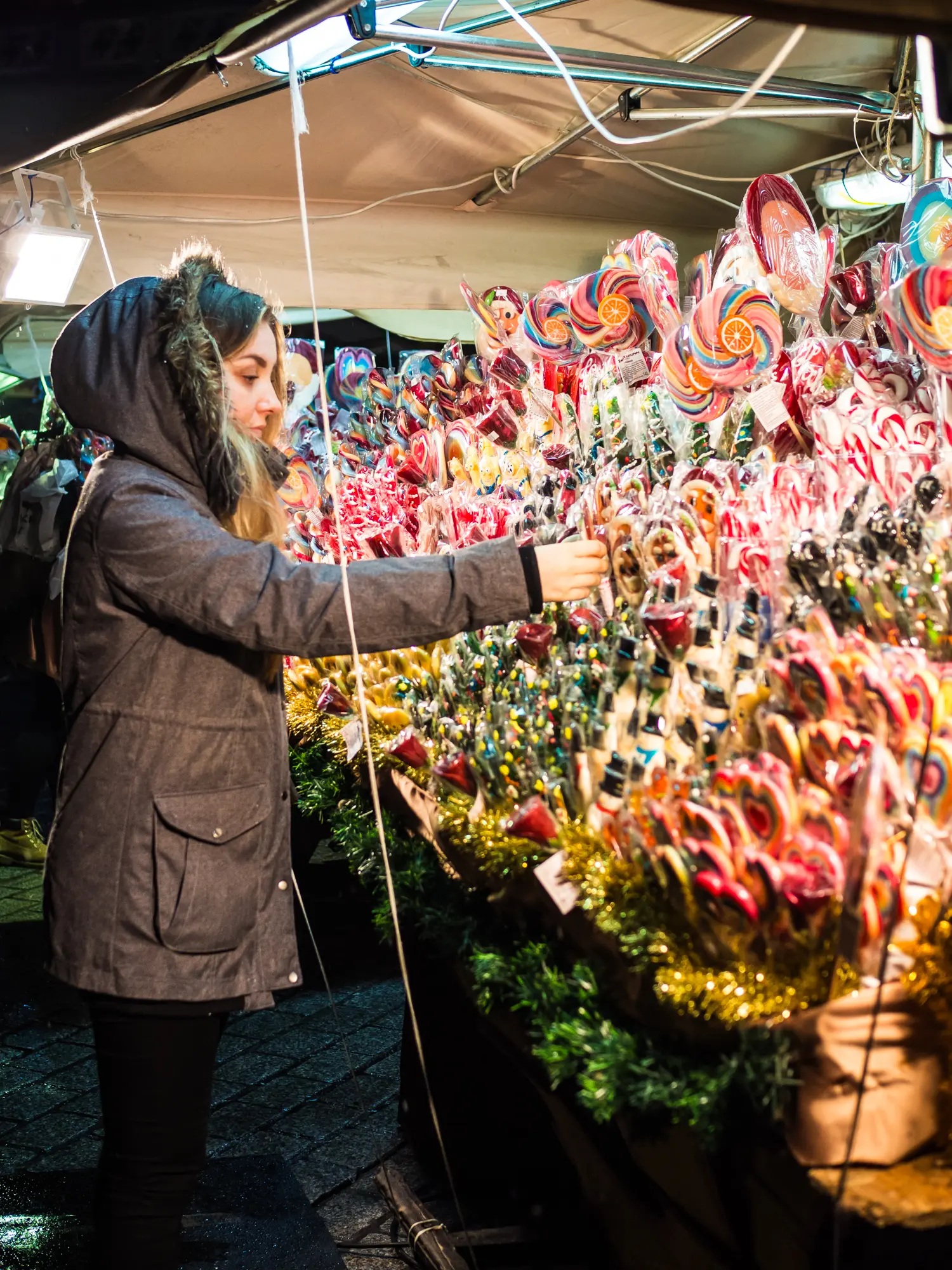 Woman wearing a grey jacket looking at lollipops at a candy stall at Krakow Christmas Market.