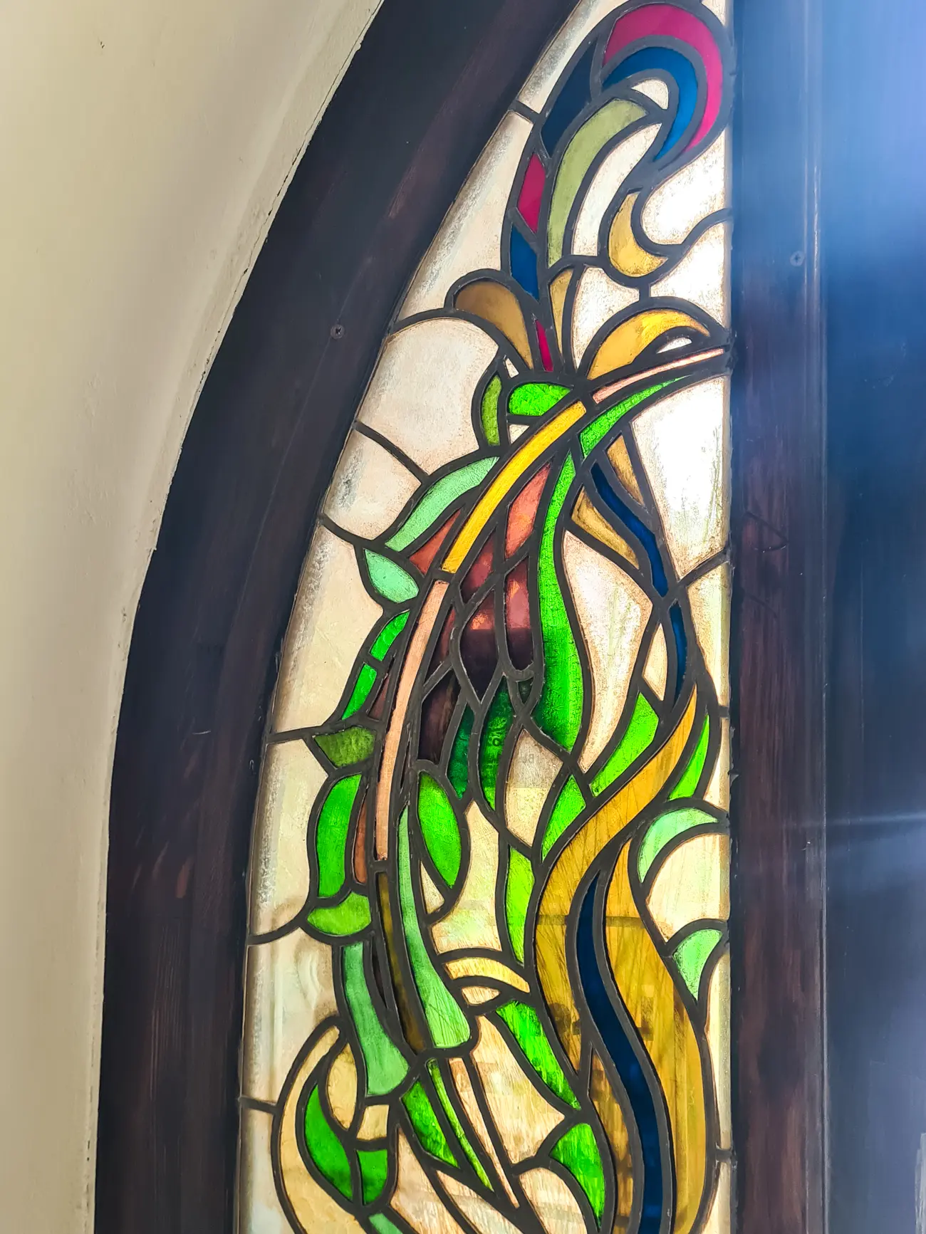 Half of an arched stained glass window with green, brown an yellow colors at the Stained Glass Museum, a hidden gem in Krakow.