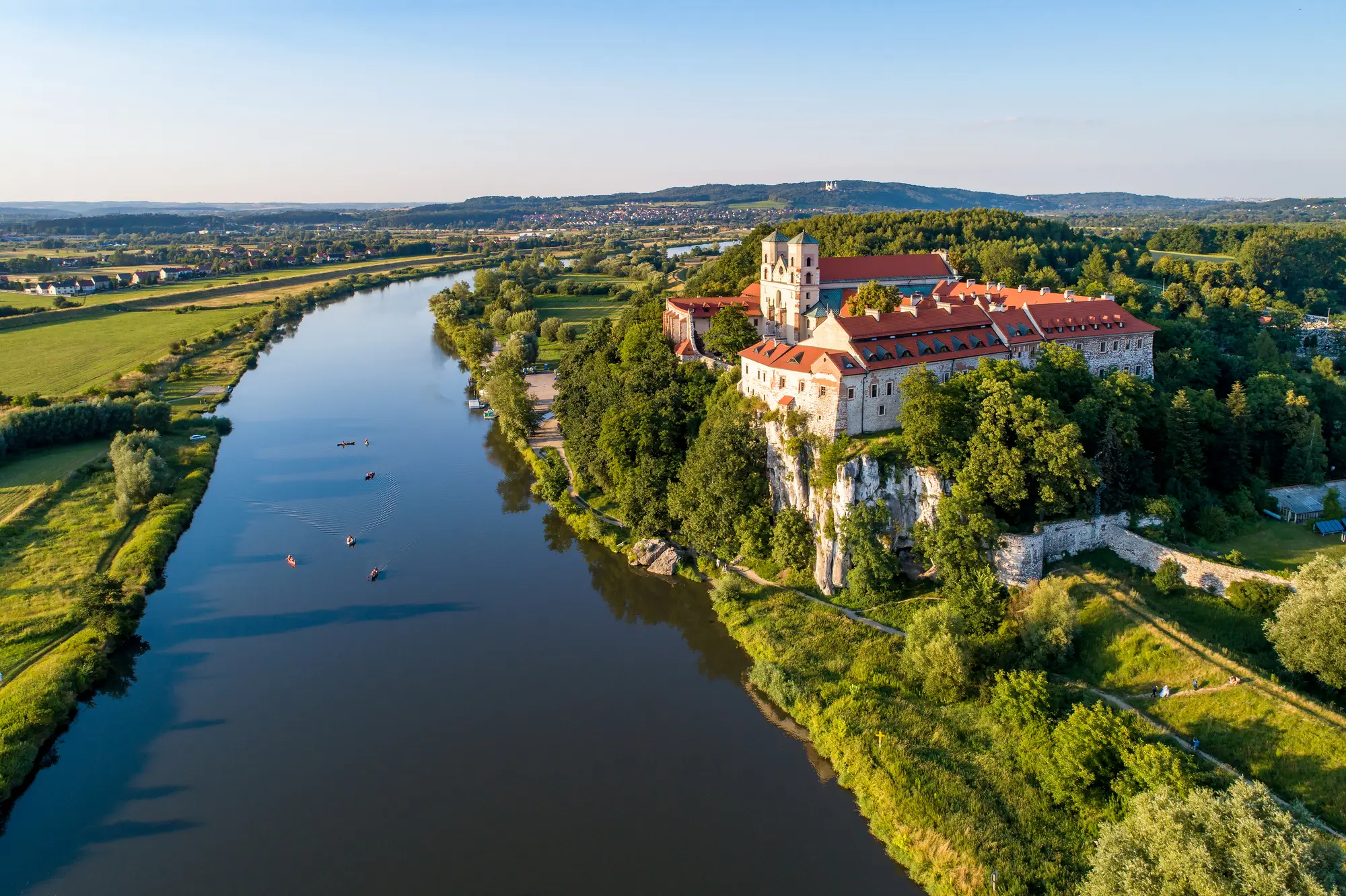 Blue river with green fields on both side with the white Tyniec Abbey on a hill on the right side, one of the most beautiful hidden gems in Krakow.