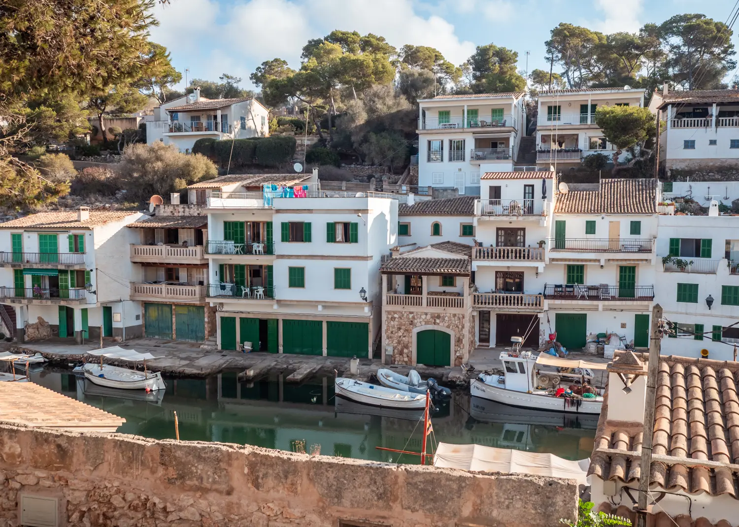 White and sandstone colored fisherman's houses with green shutters and doors on a hillside in Cala Figuera Port on Mallorca.