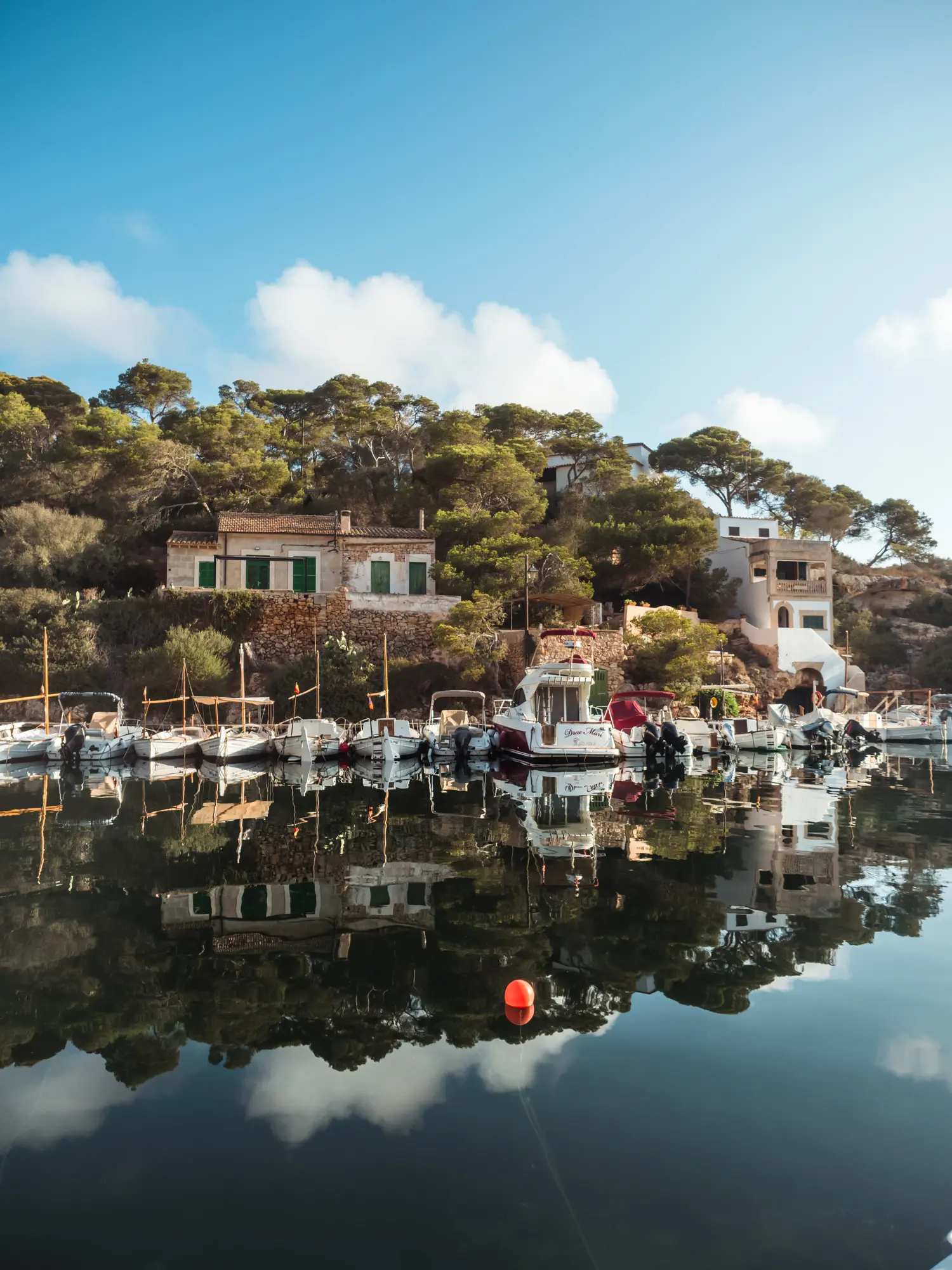 Boats and old fisherman's houses with green doors reflecting in the calm sea on a sunny morning in Cala Figuera Mallorca.