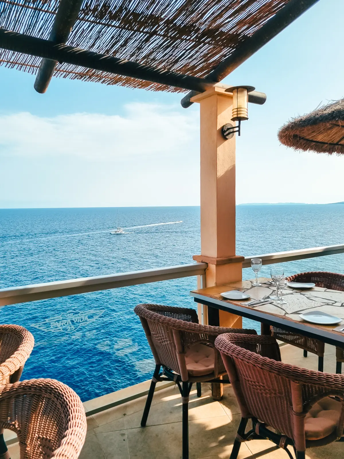 A set table with brown chairs on a covered patio overlooking the ocean at Pura Vida Restaurant in Cala Figuera.