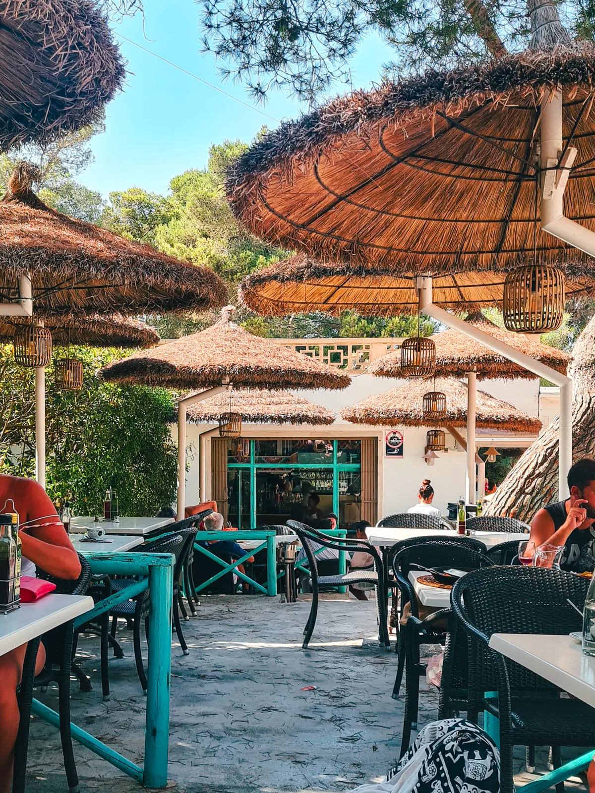 Turquoise tables and straw parasols at Sa Font de n'Alis restaurant in Cala Mondrago, Mallorca.