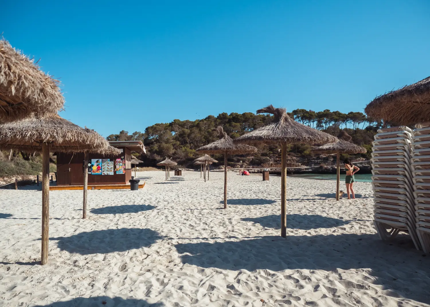 Straw parasols and a stack of white plastic sunbeds at the white-sand Cala S'Amarador in Mondrago Natural Park, one of the best beaches in Mallorca.