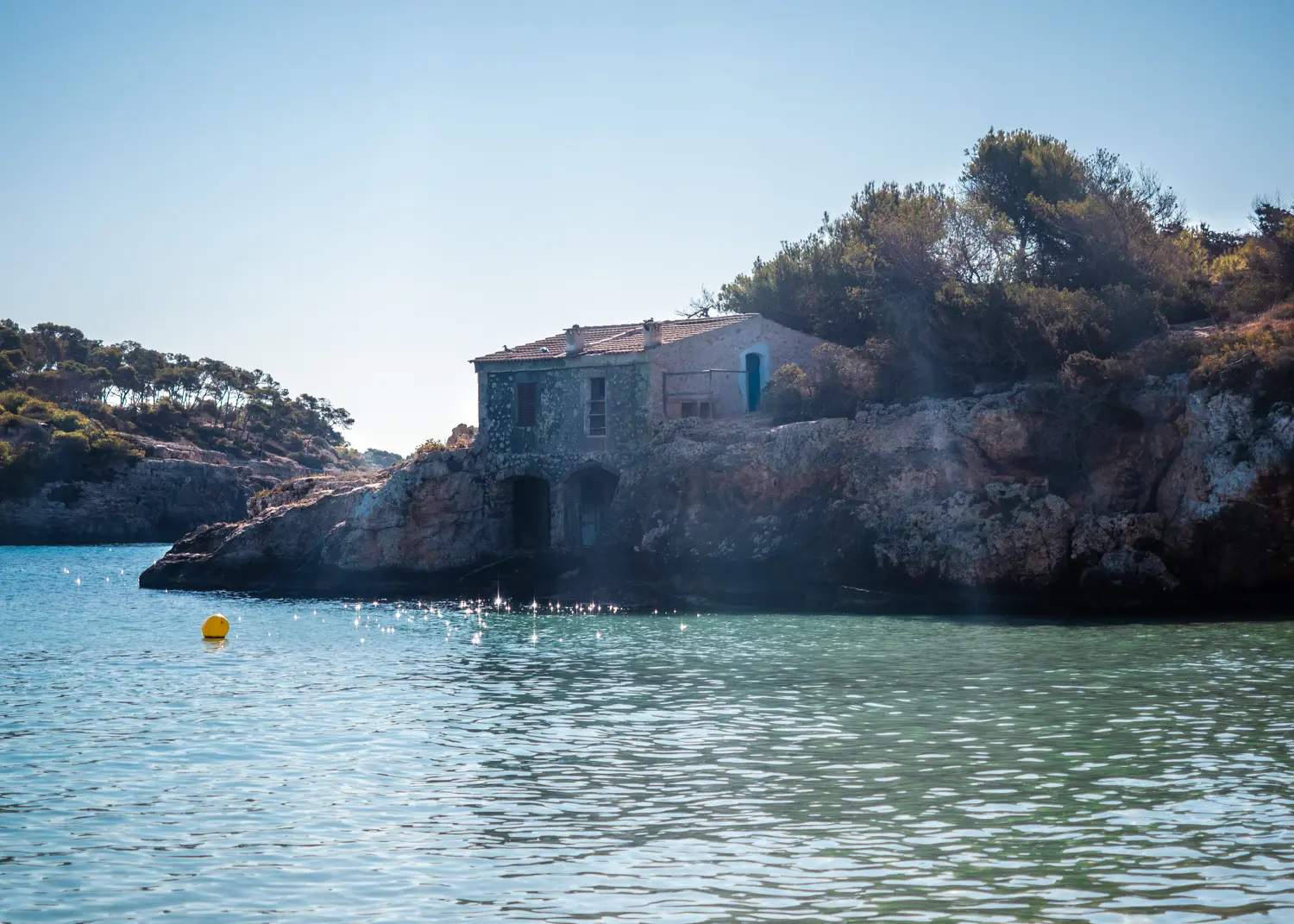 Old stone fisherman's house with dark blue doors down by the turquoise ocean at Cala S'Amarador, one of the best beaches in Mallorca.
