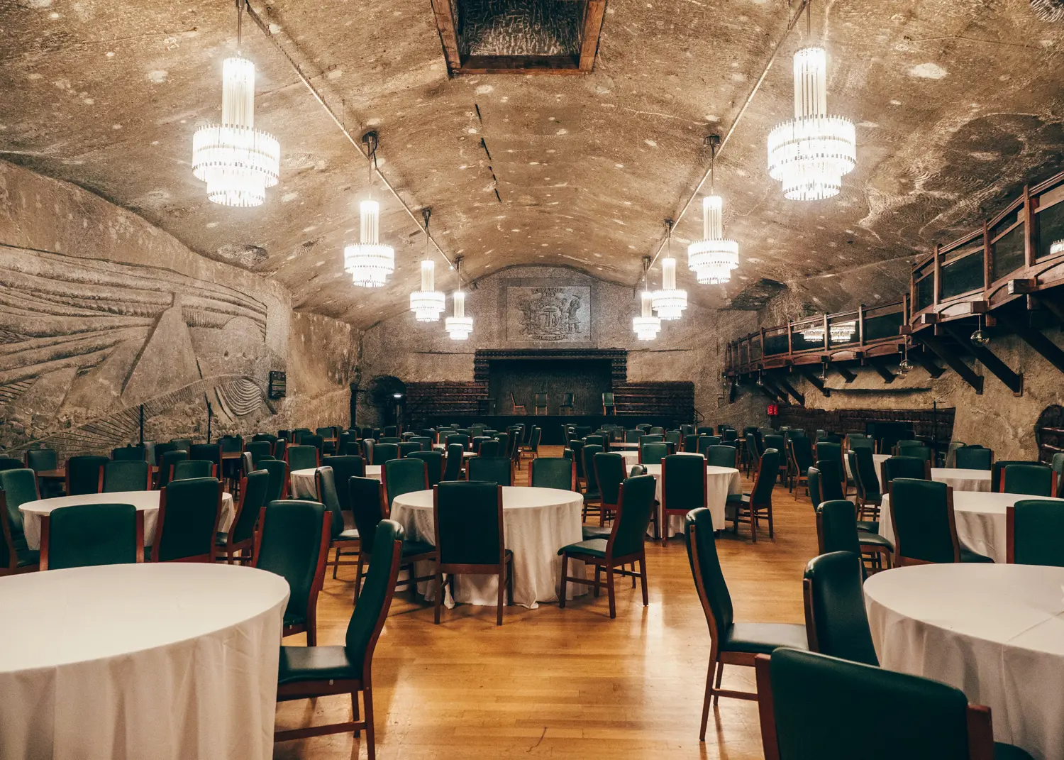Round tables with white tablecloths and green chairs in a large event space inside Wieliczka Salt Mine in Krakow.