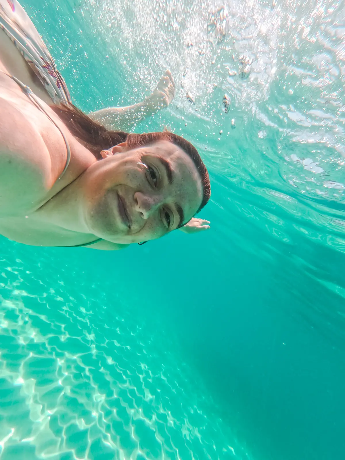 Girl with dark hair swimming under water in the turquoise ocean of Cala S'Amarador in Mondrago Natural Park in Mallorca.