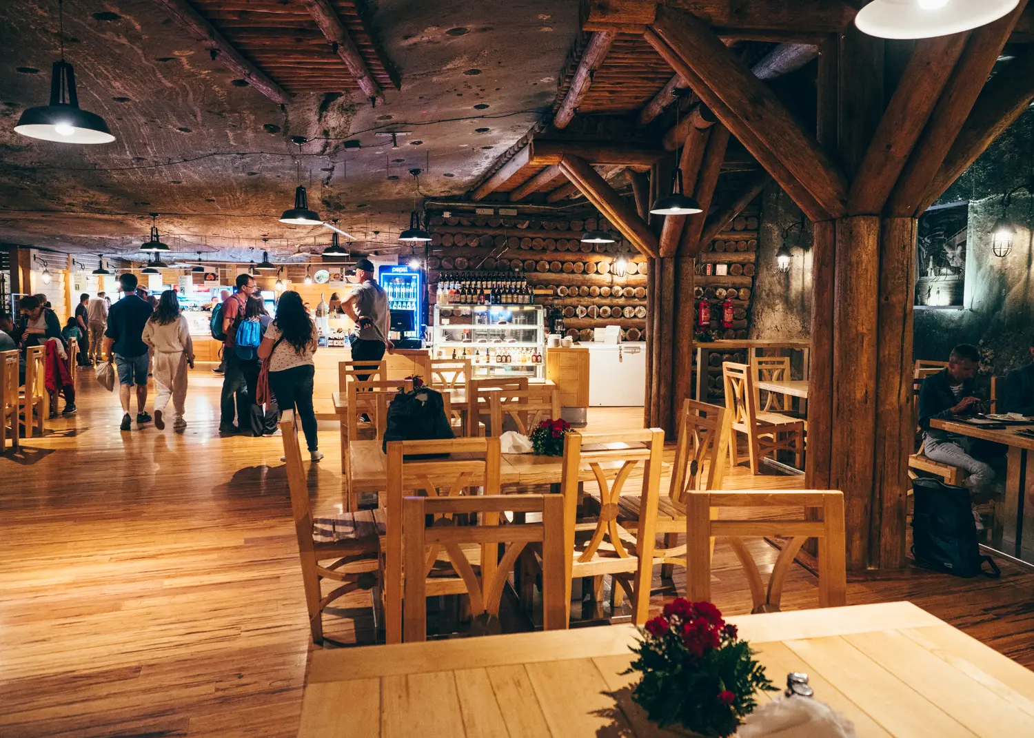 Wooden tables and chairs with people standing in line in the background in the restaurant in Wieliczka Salt Mine.