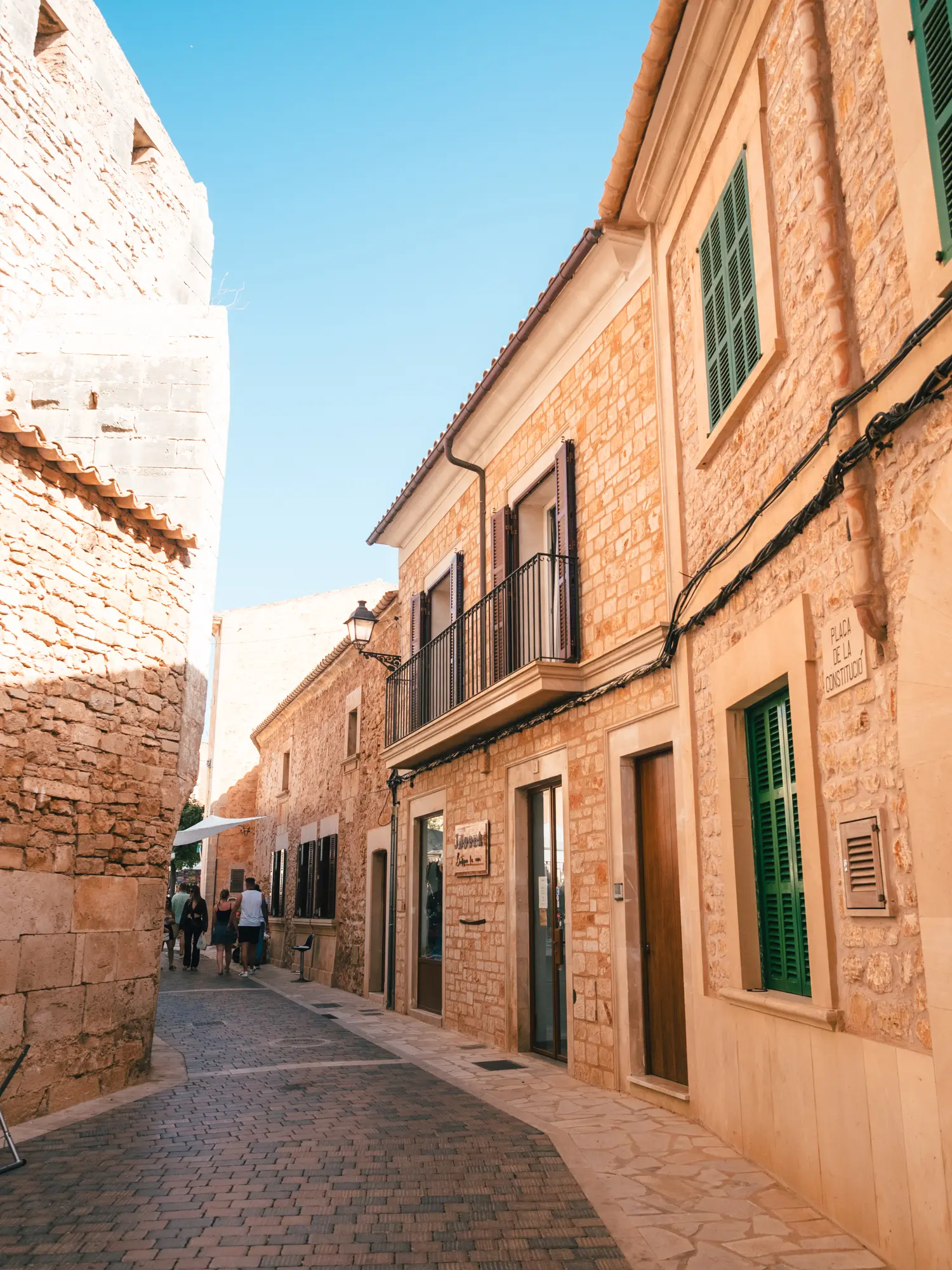 Narrow cobbled road between sandstone houses with green doors and shutters in Santanyi Mallorca.