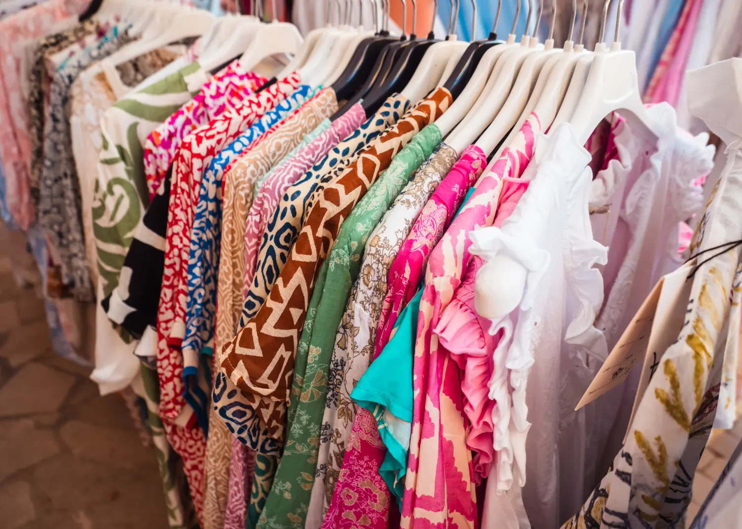 Row of colorful patterned dresses on white hangers at Santanyi Market in Mallorca.