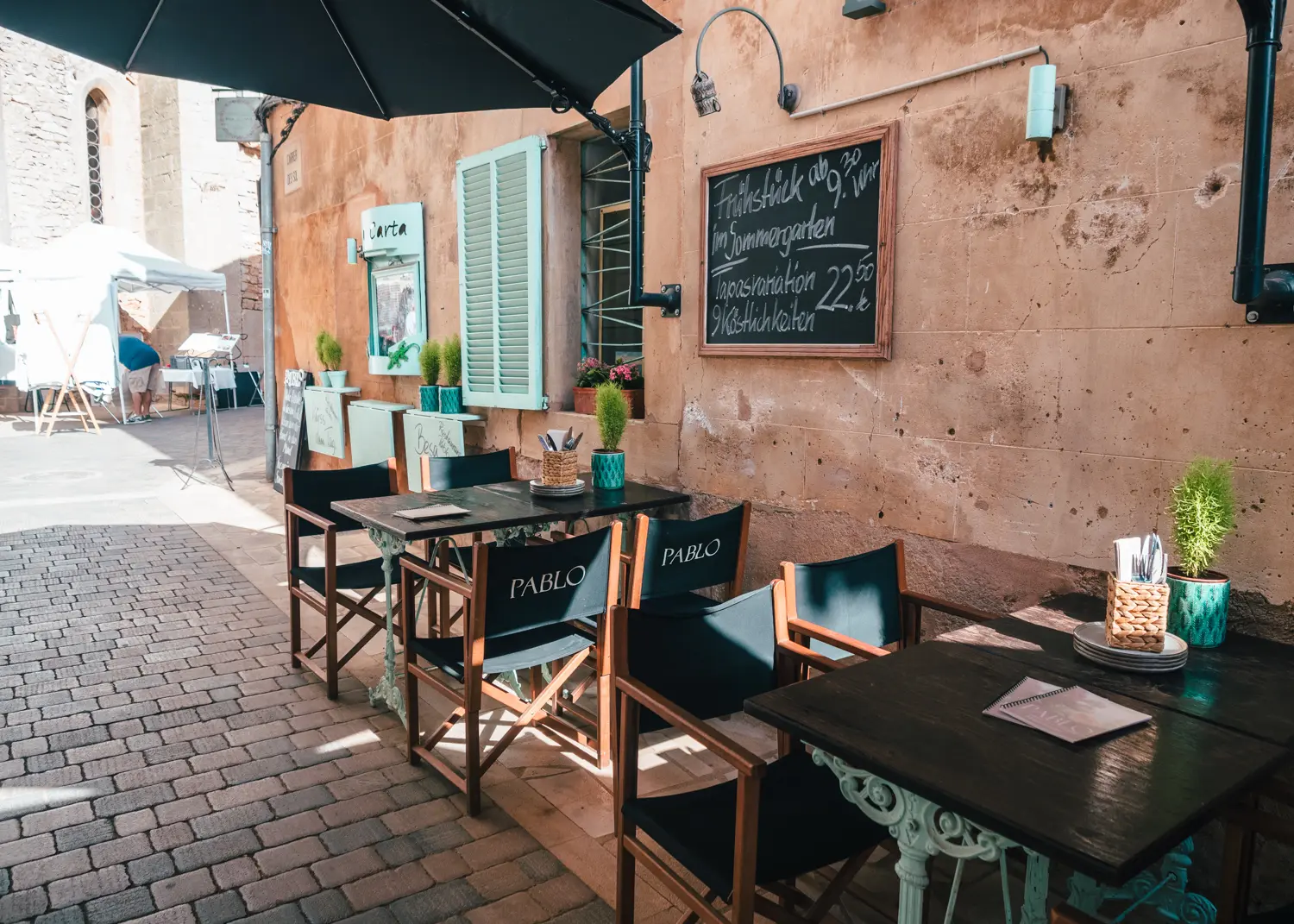 Pablo restaurants in a sandstone building with turquoise shutters in Santanyi with tables close to the wall in a narrow cobbled street.