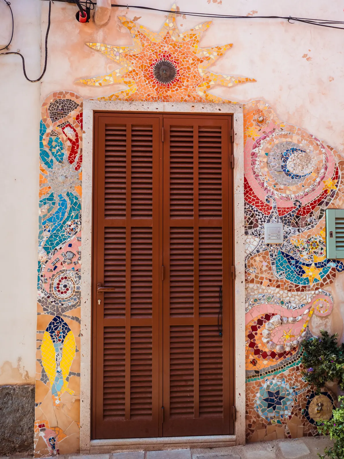 Brown door surrounded by a colorful mosaic artwork with a sun op top in Santanyi Mallorca.