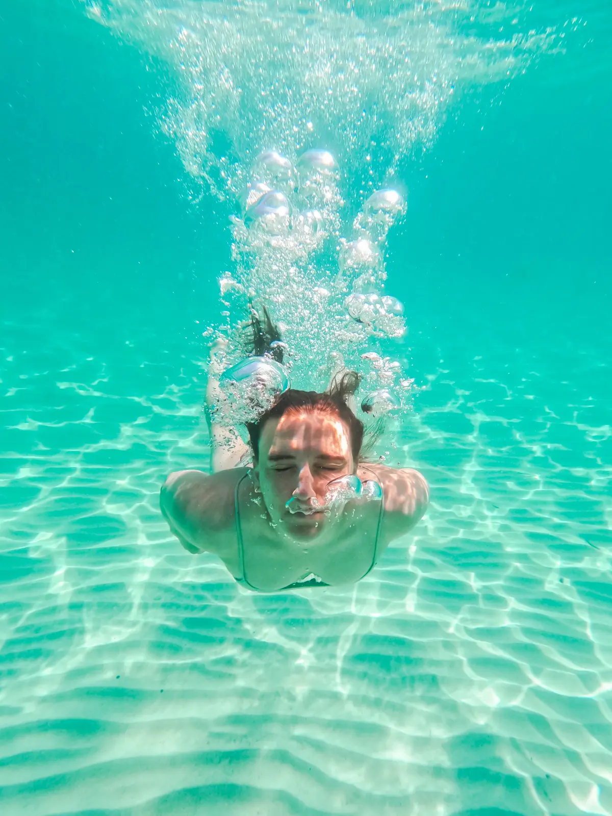 Girl swimming under turquoise water blowing bubbles with the sun shining down, in Mondrago Natural Park, Mallorca.