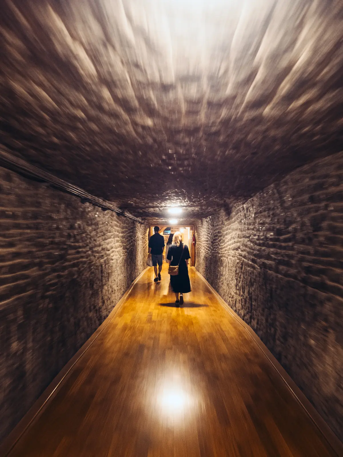 Woman wearing a long black dress walking through the exit tunnel with wooden floor and stone ceiling in Wieliczka Salt Mine.