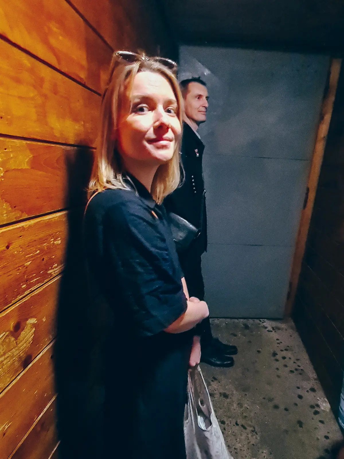 Woman with blonde wearing, wearing a long black dress, standing in a wooden tunnel waiting to enter Wieliczka Salt Mine with our guide.