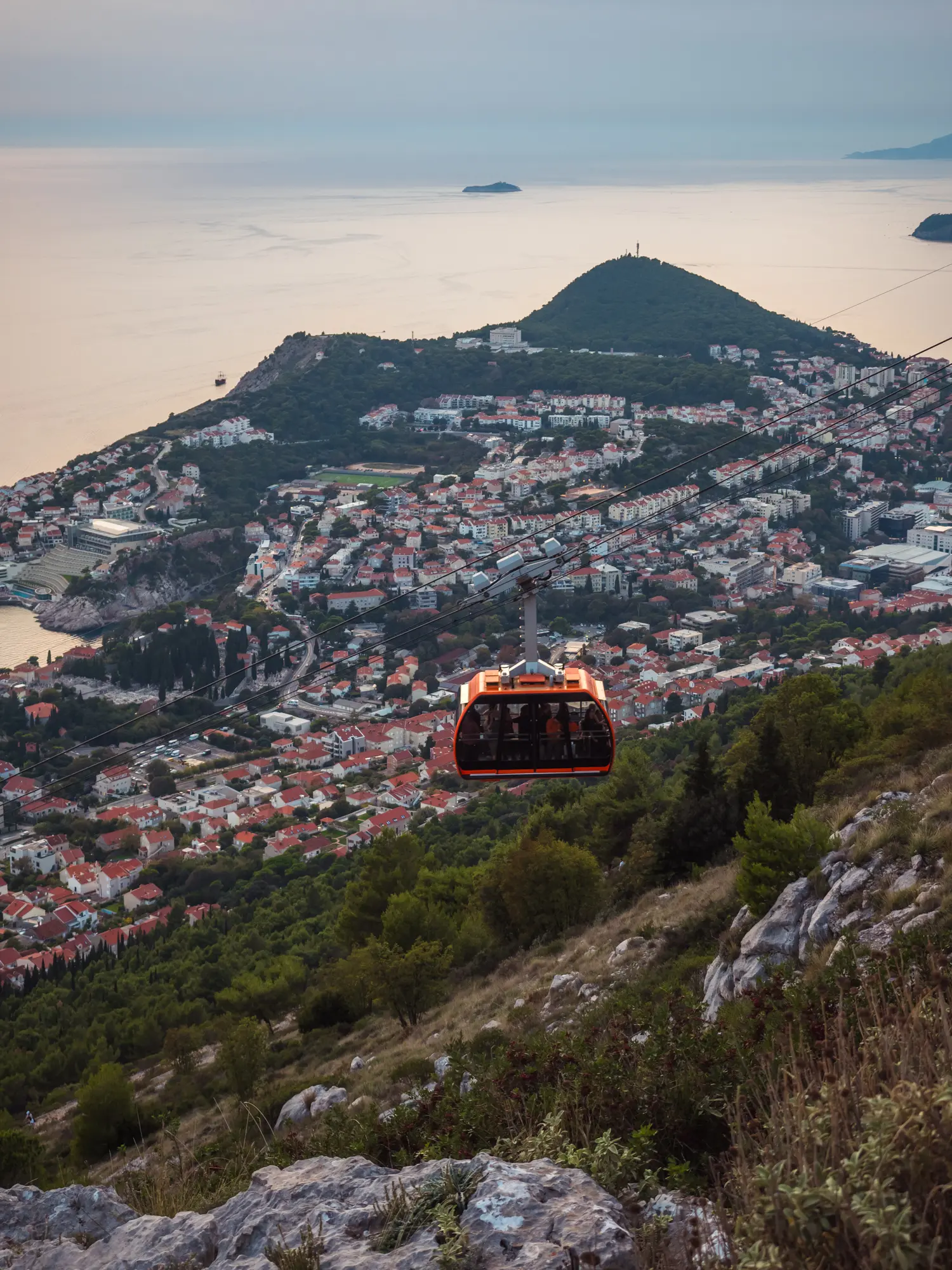 Orange cable car to Mount Srd, with the sun setting over Dubrovnik and the ocean in the background. Is the cable car worth it?