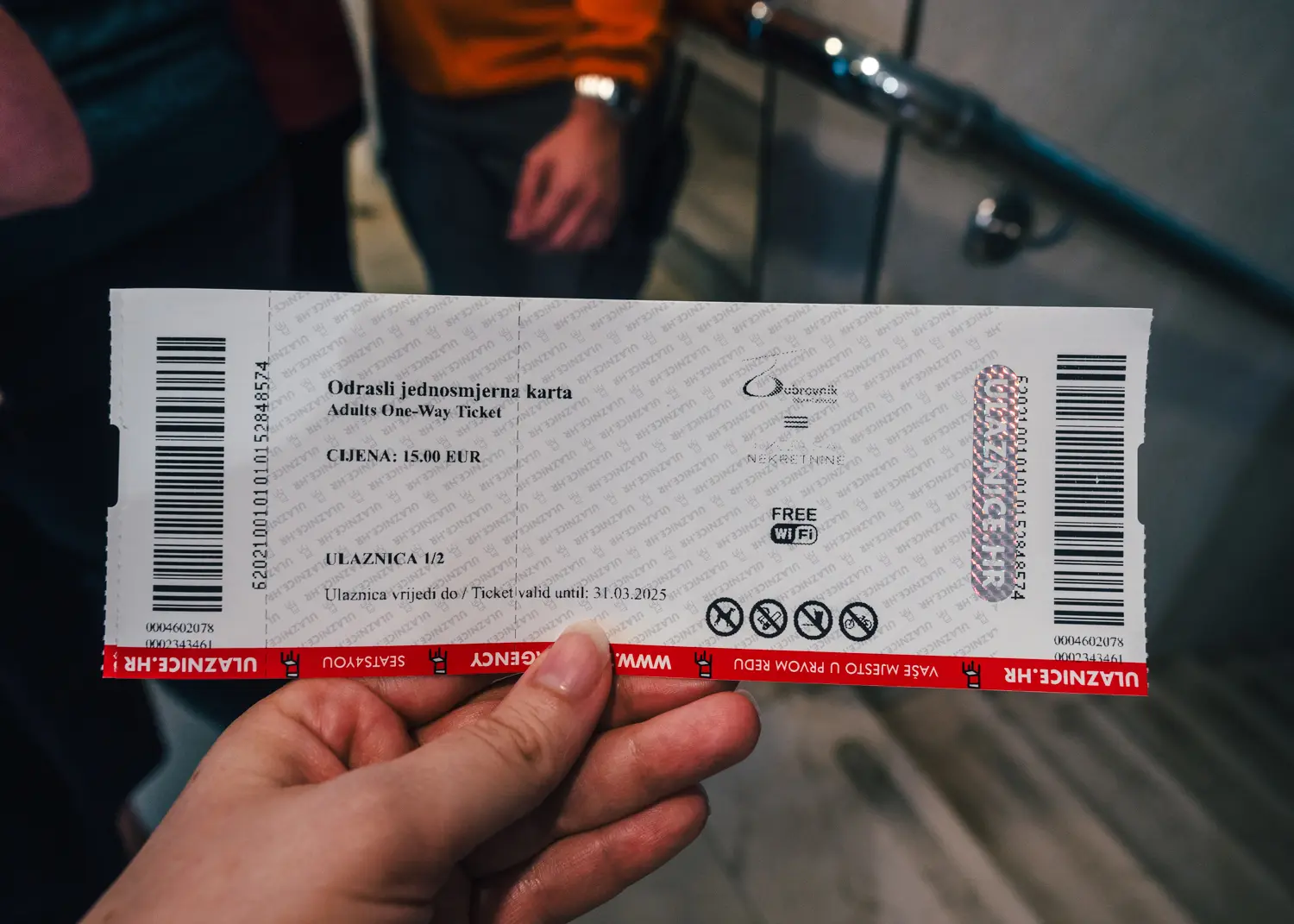 Close up of a hand holding a red and white ticket for the cable car in Dubrovnik, how to get to Mount Srd.