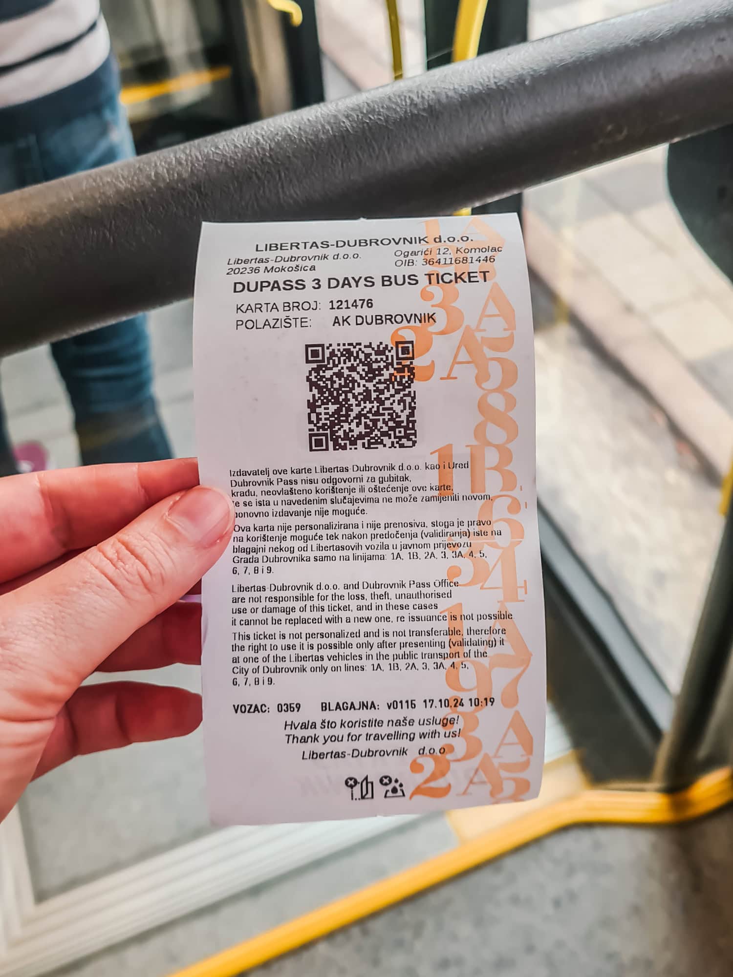 Hand holding a white paper 3-day bus ticket as part of the Dubrovnik Card inside a bus.
