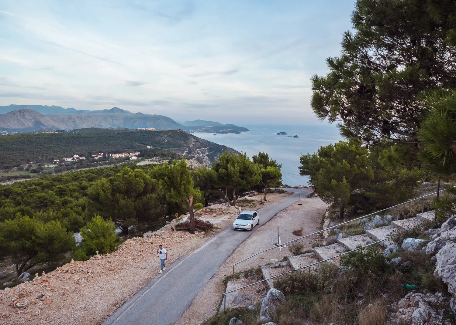 White car driving to the top of Mount Srd in Dubrovnik with green mountains and the ocean in the background at dusk. Mount Srd transportation.