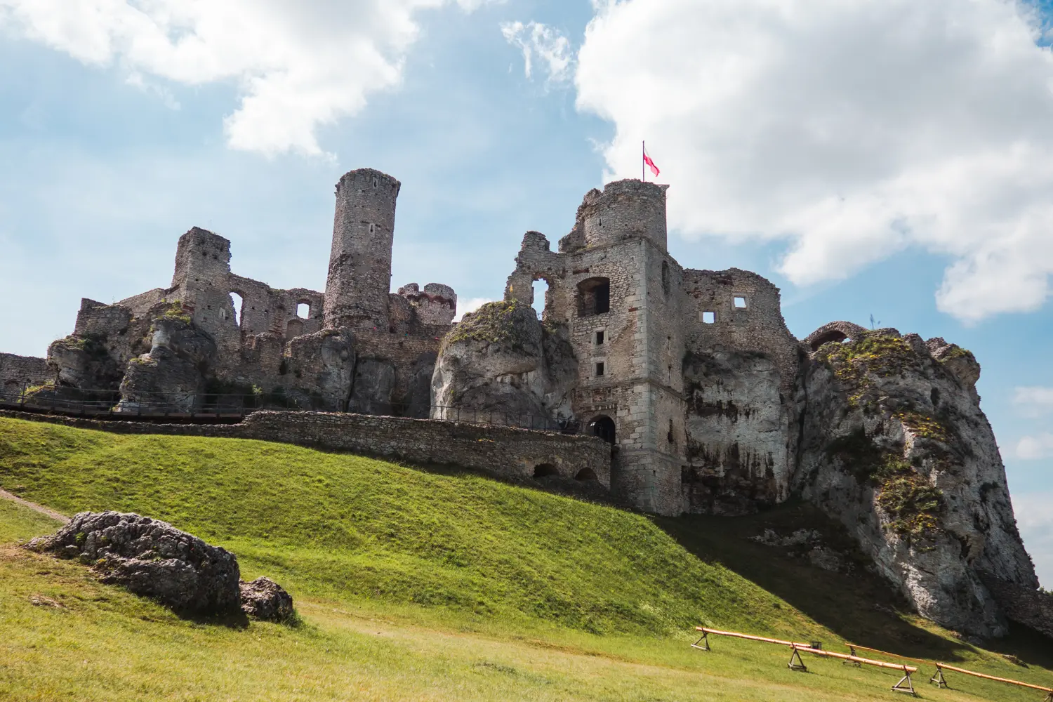 Looking towards Ogrodzieniec Castle ruin with towers and a flag on a hill, surrounded by green grass, close to Krakow.