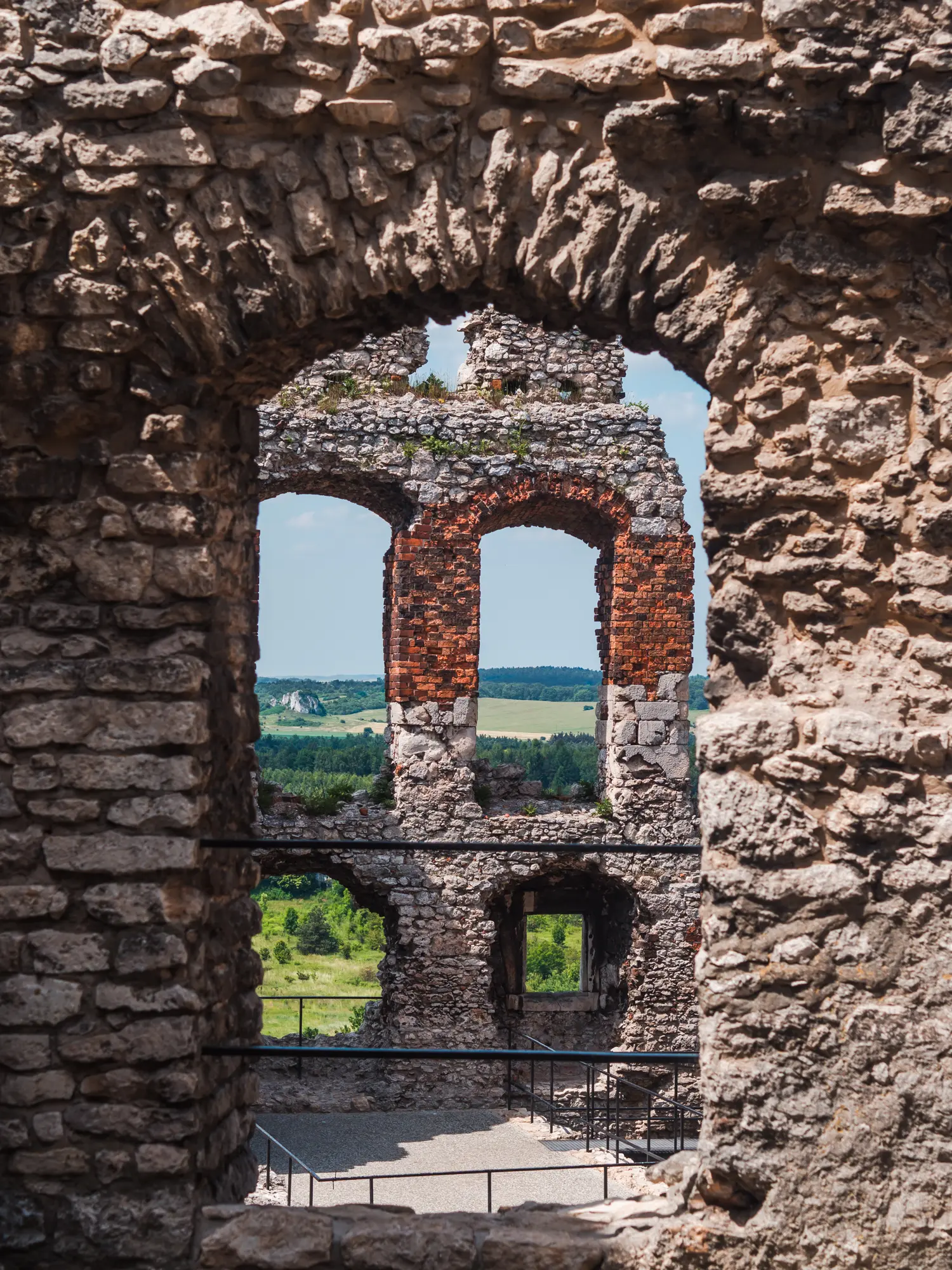 Arched opening in a stone ruin wall looking onto another wall with many arched windows at Ogrodzieniec Castle ruin, a haunted castle in Poland.