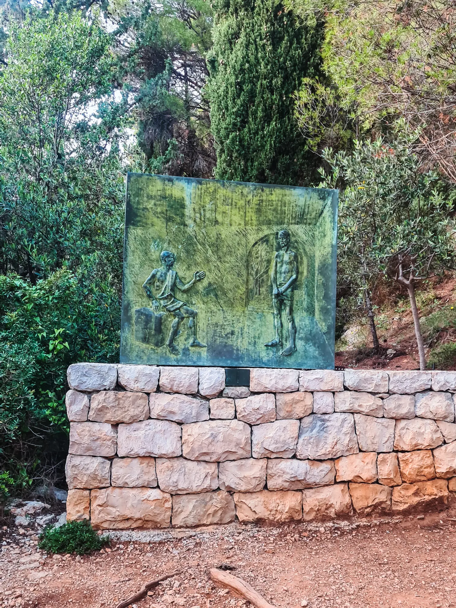 Square metal artwork on a stone wall with green trees in the background, showing the way to Mount Srd viewpoint Dubrovnik.