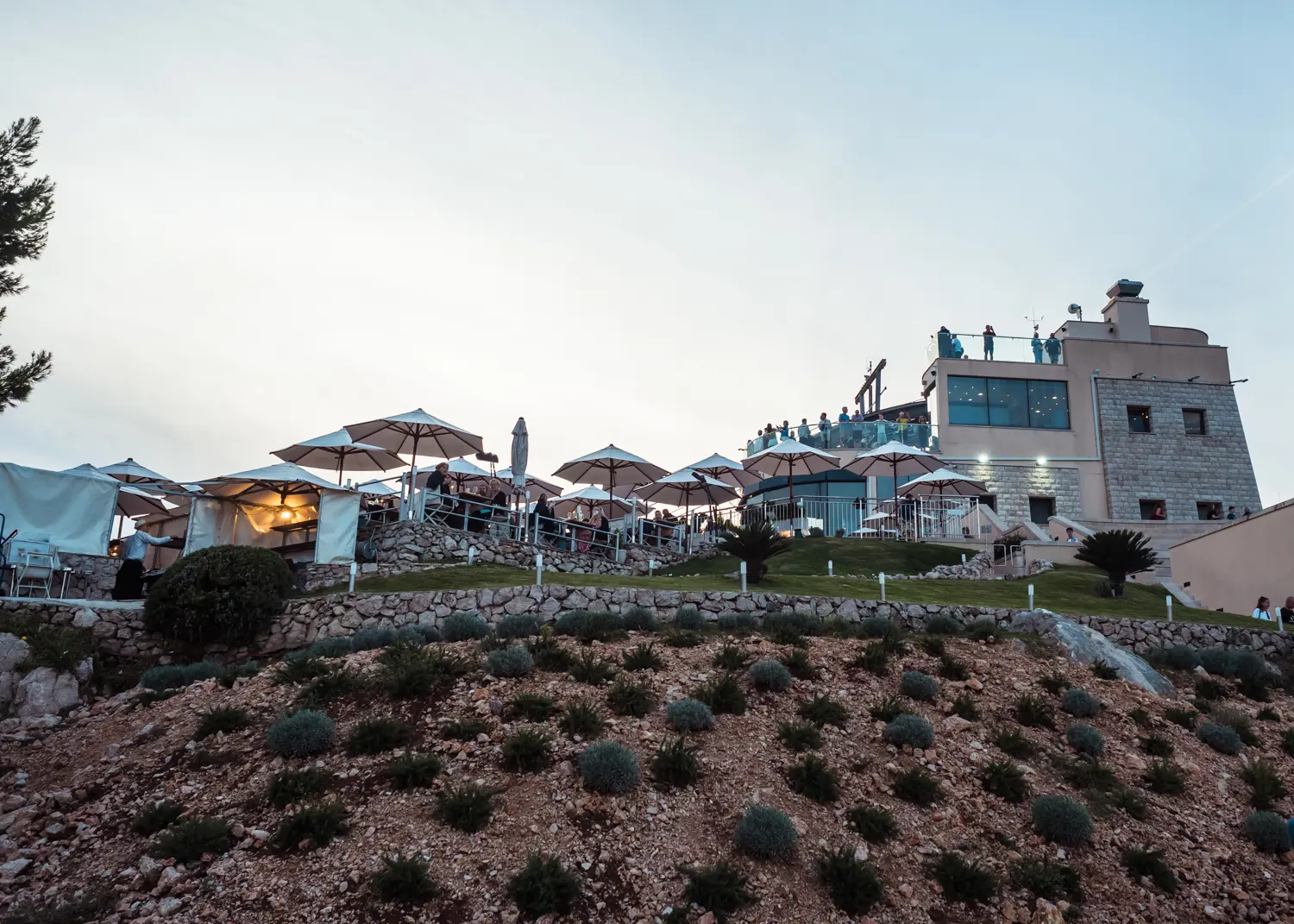 View from below of Panorama Restaurant & Bar on a hill with many parasols and the cable car building in the background on Mount Srd in Dubrovnik.