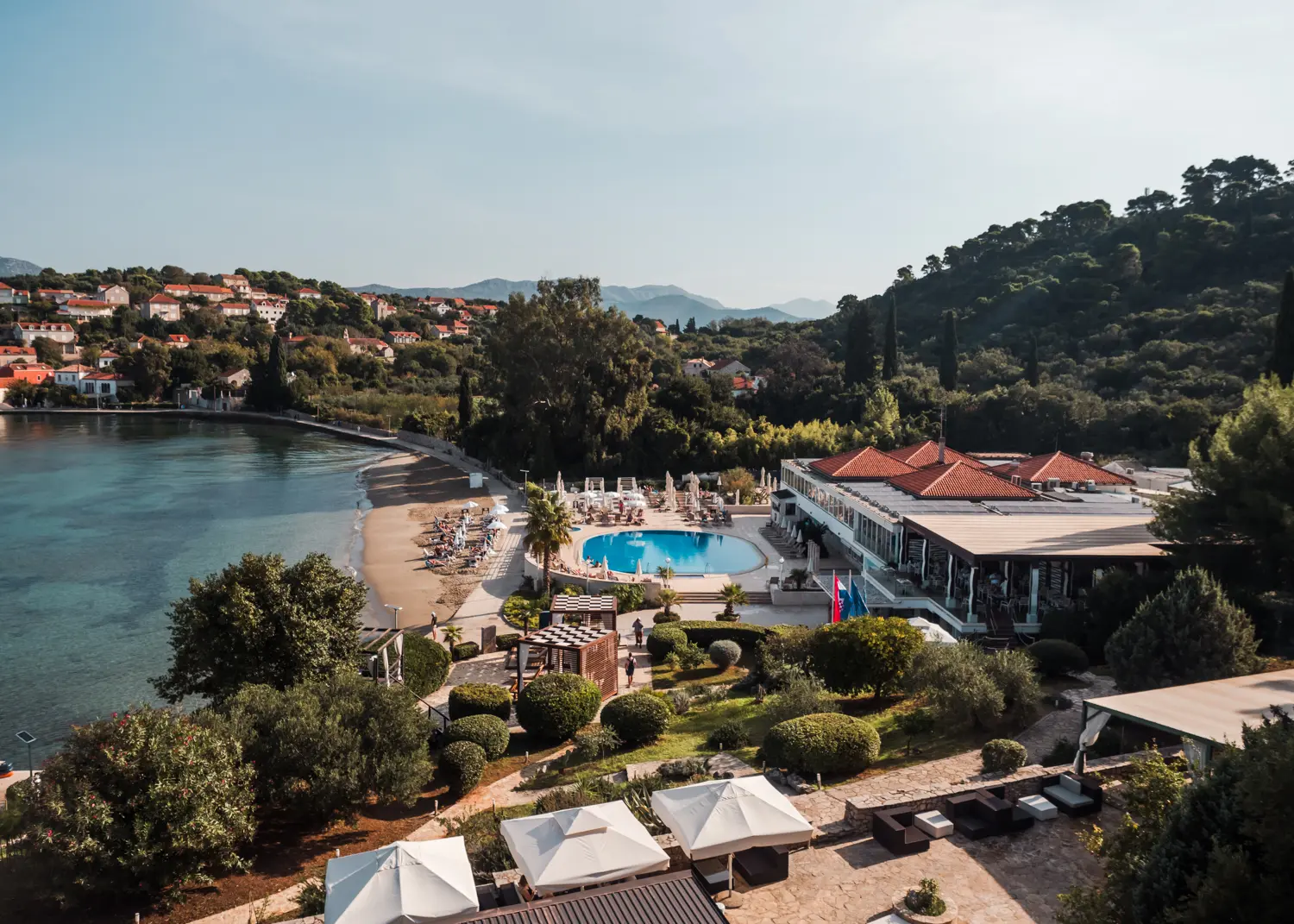 View of a round turquoise poos and orange rooftops of TUI BLUE resort on the beach surrounded by green trees on Kolocep Island, Dubrovnik.
