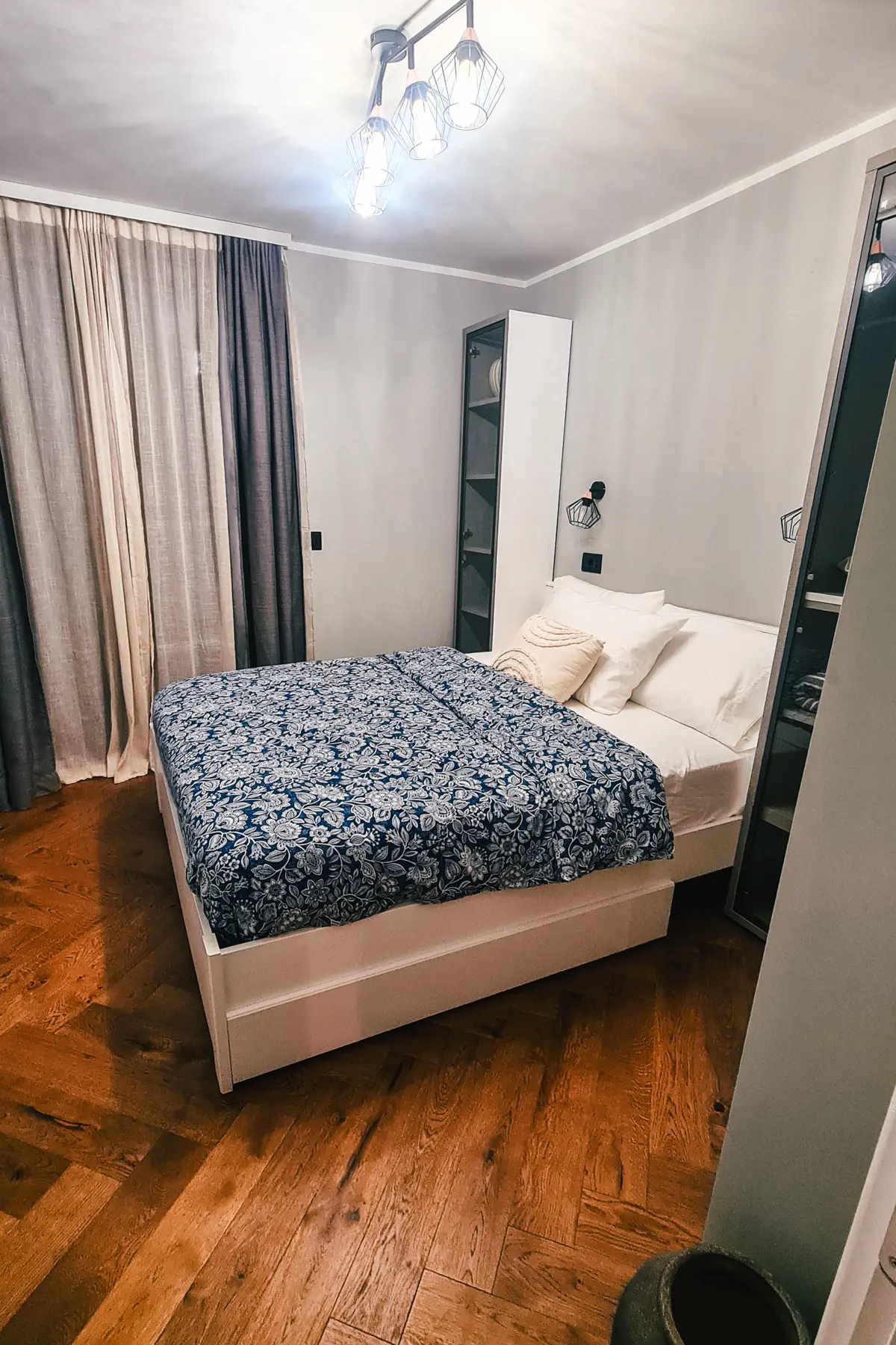 White bed with blue and white patterned bedspread in a light grey room with warm herringbone floors in the best apartment to stay in Dubrovnik.