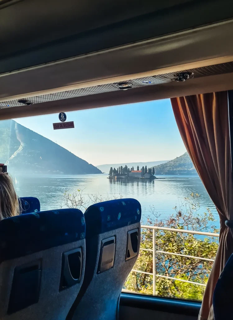 Looking out a bus window, past two blue bus seats, on a small islet in the middle of Bay of Kotor, on the way from Dubrovnik to Kotor by bus.