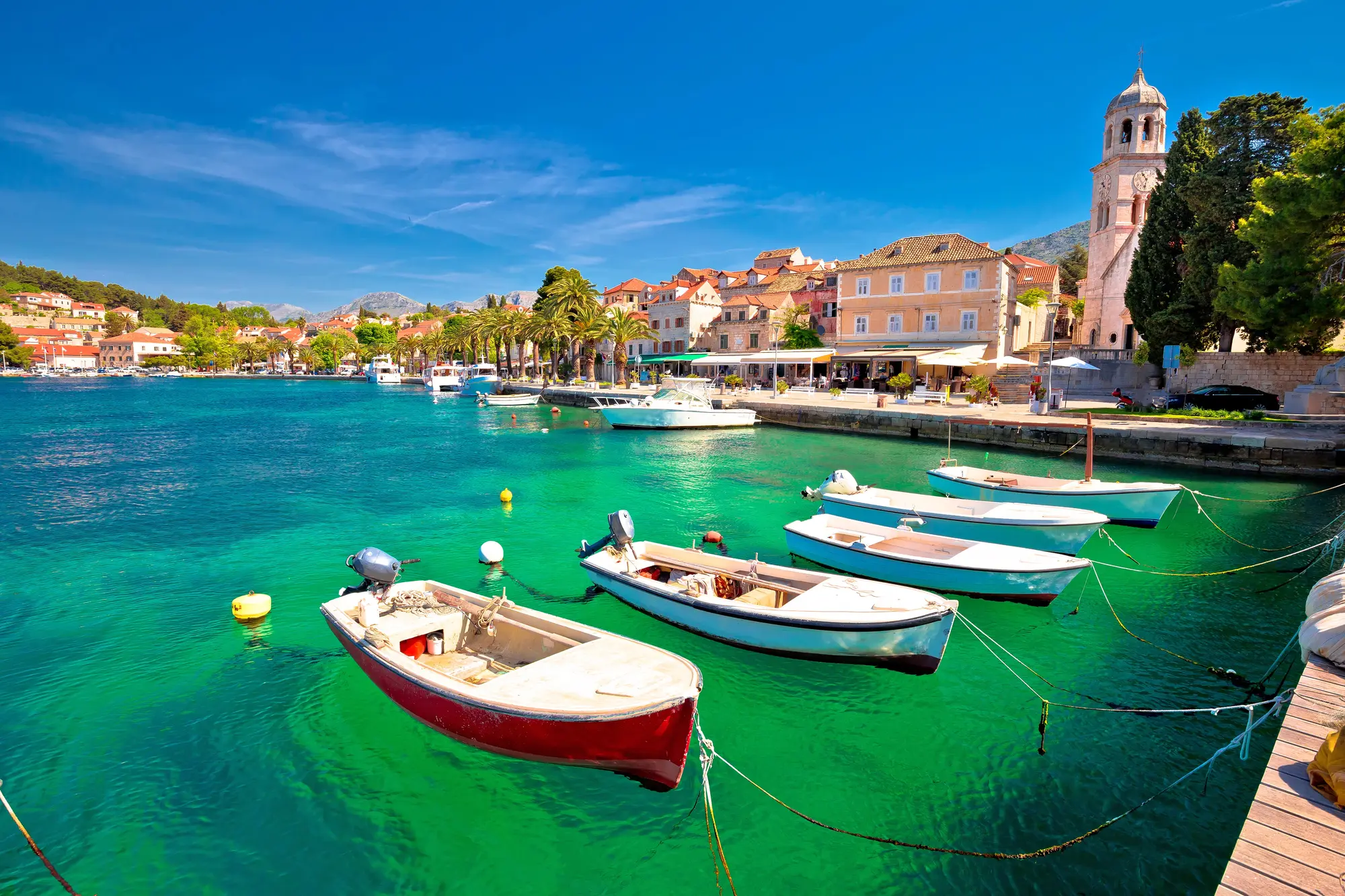 Small red and blue boats on clear green water in front of beige stone houses along the harbor in Cavtat during a Dubrovnik highlights tour.