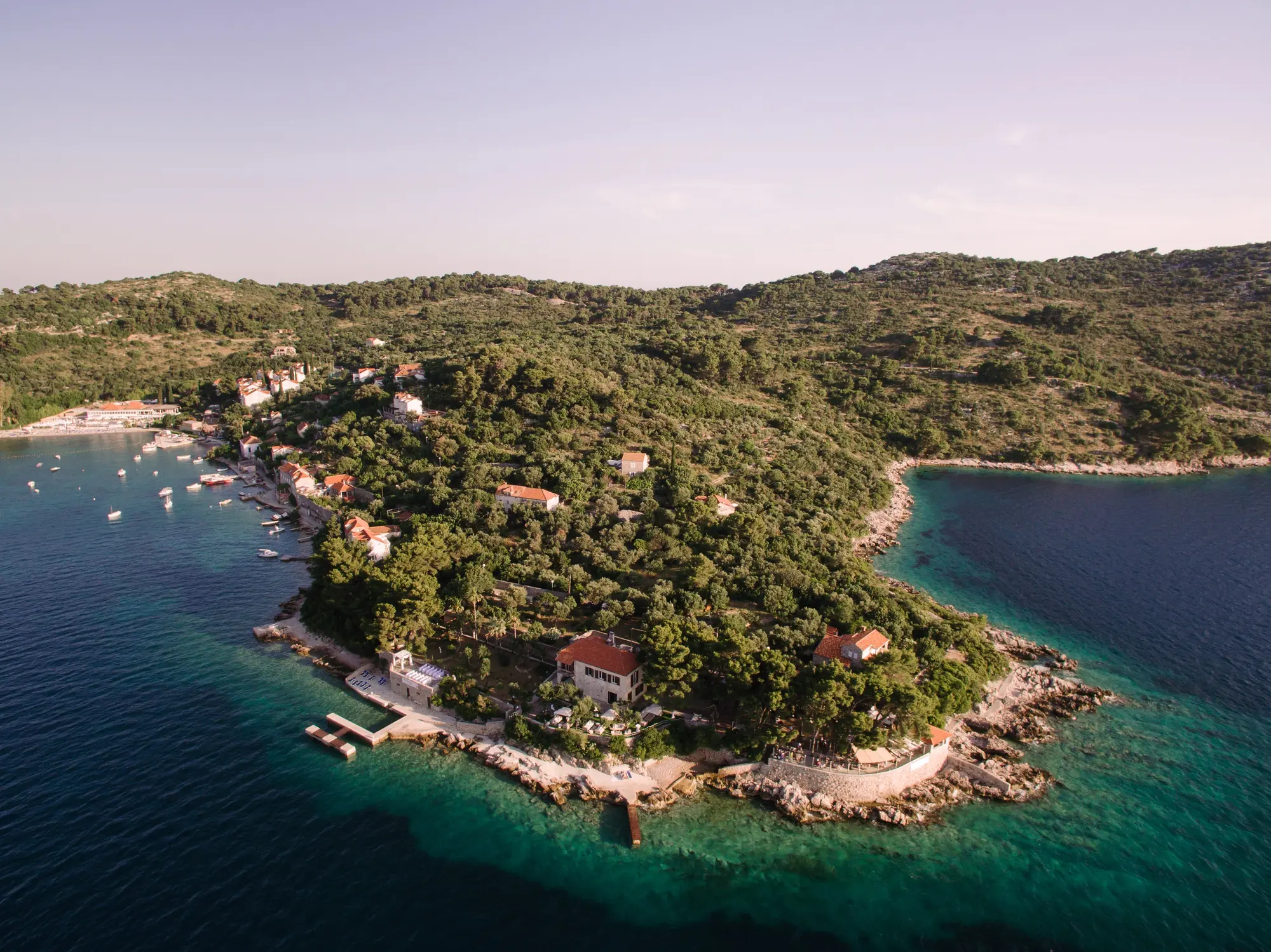 Drone view of an outcrop covered in greenery with TUI BLUE Kalamota Island Resort in the background on Kolocep Island.