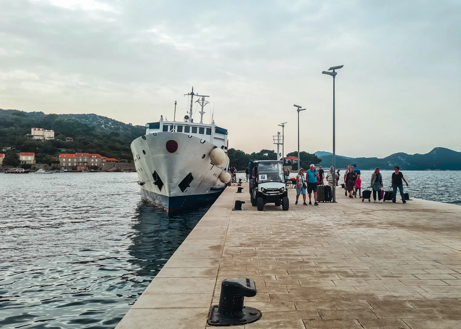 People walking from a white ferry coming from Dubrovnik on a stone pier in Koločep, Elaphiti Islands.