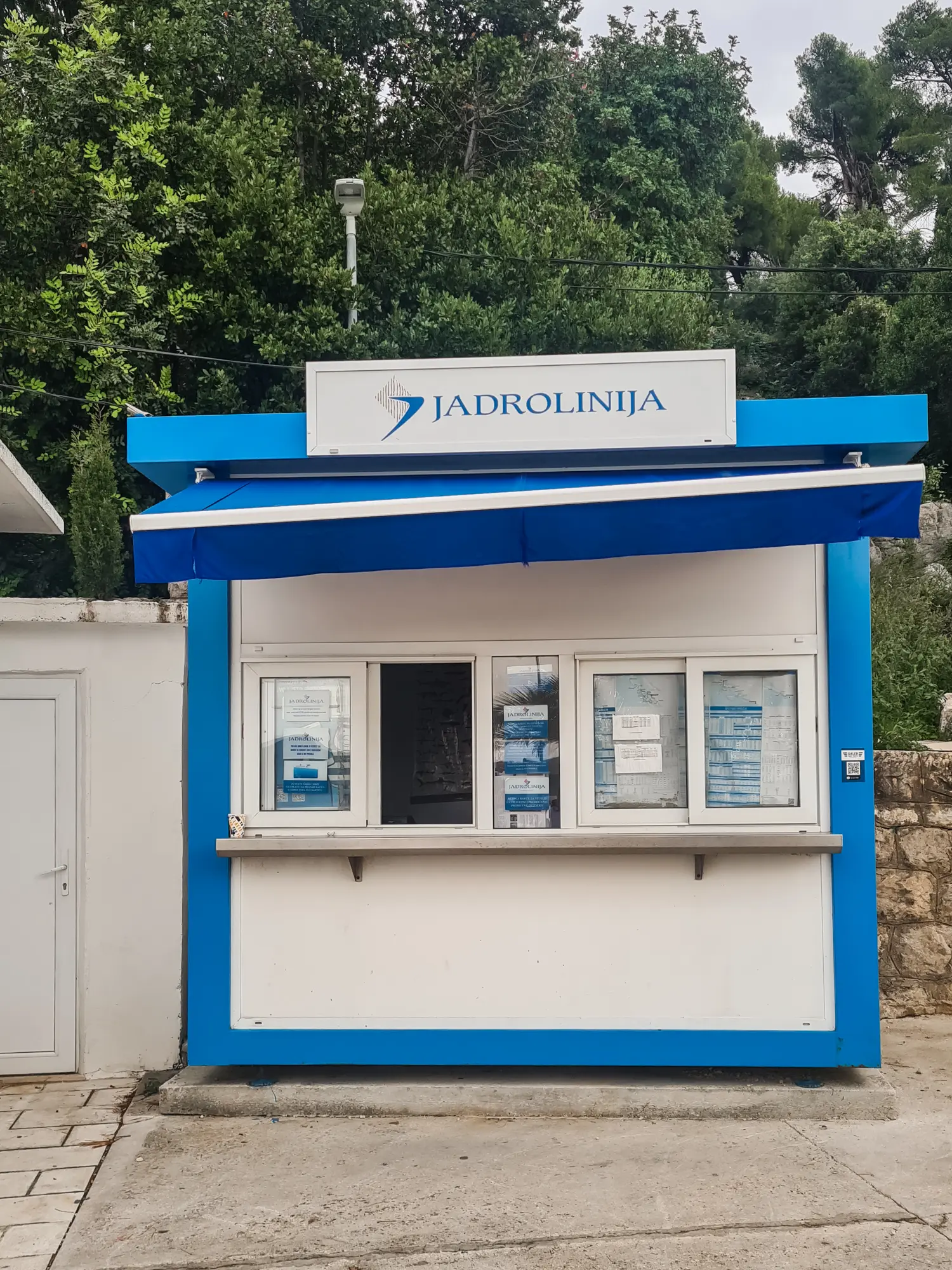 White box with blue trim and a ticket window selling tickets for the Elaphiti Islands to Dubrovnik ferry on Kolocep Island.