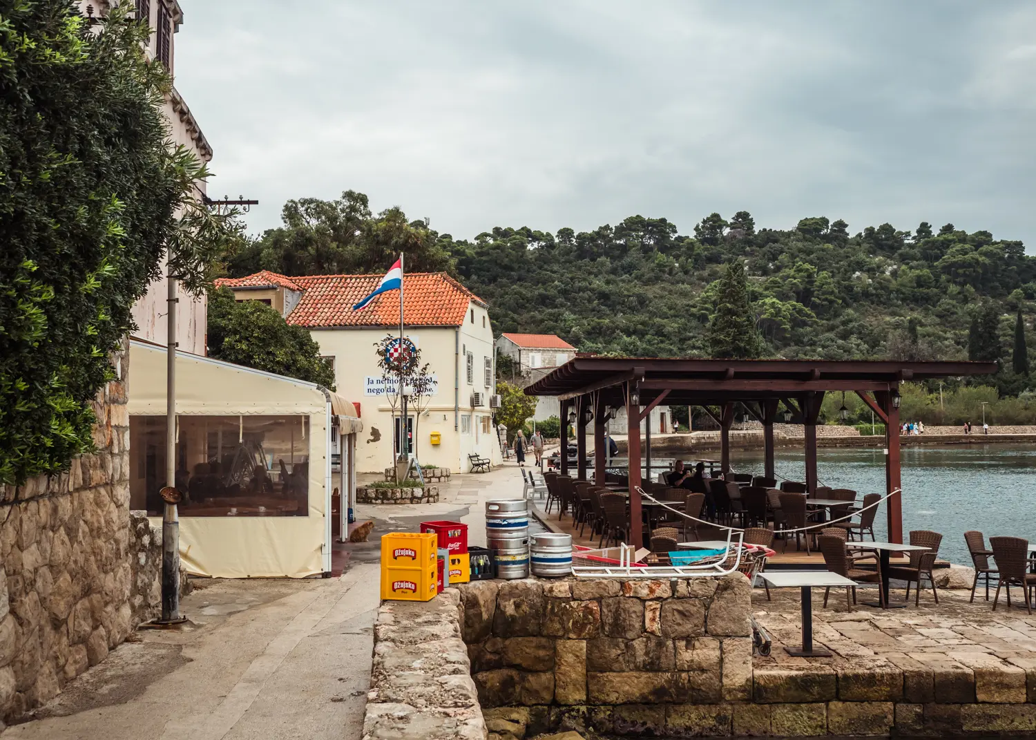 Restaurant with seating under a brown pergola by the ocean and small market close to TUI BLUE Kalamota Island Resort on Kolocep, Dubrovnik.
