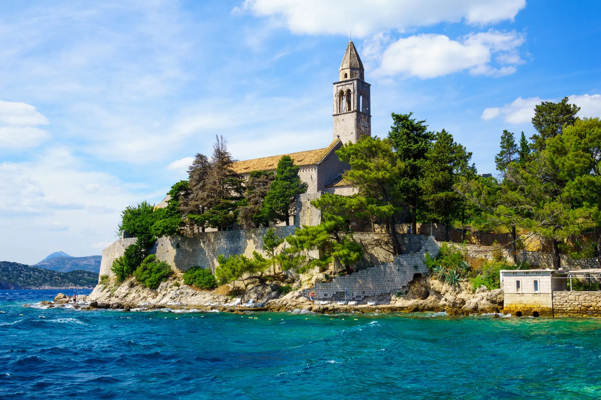 Lopud Franciscan Monastery surrounded by green trees on an outcrop on the ocean on Lopud Island, part of the Elaphiti Islands, Dubrovnik.