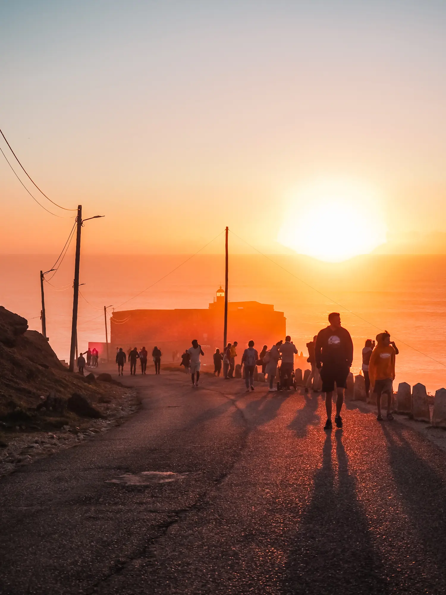 People walking up a road after watching the big waves in Nazare from Forte de São Miguel Arcanjo during a pink and orange sunset.