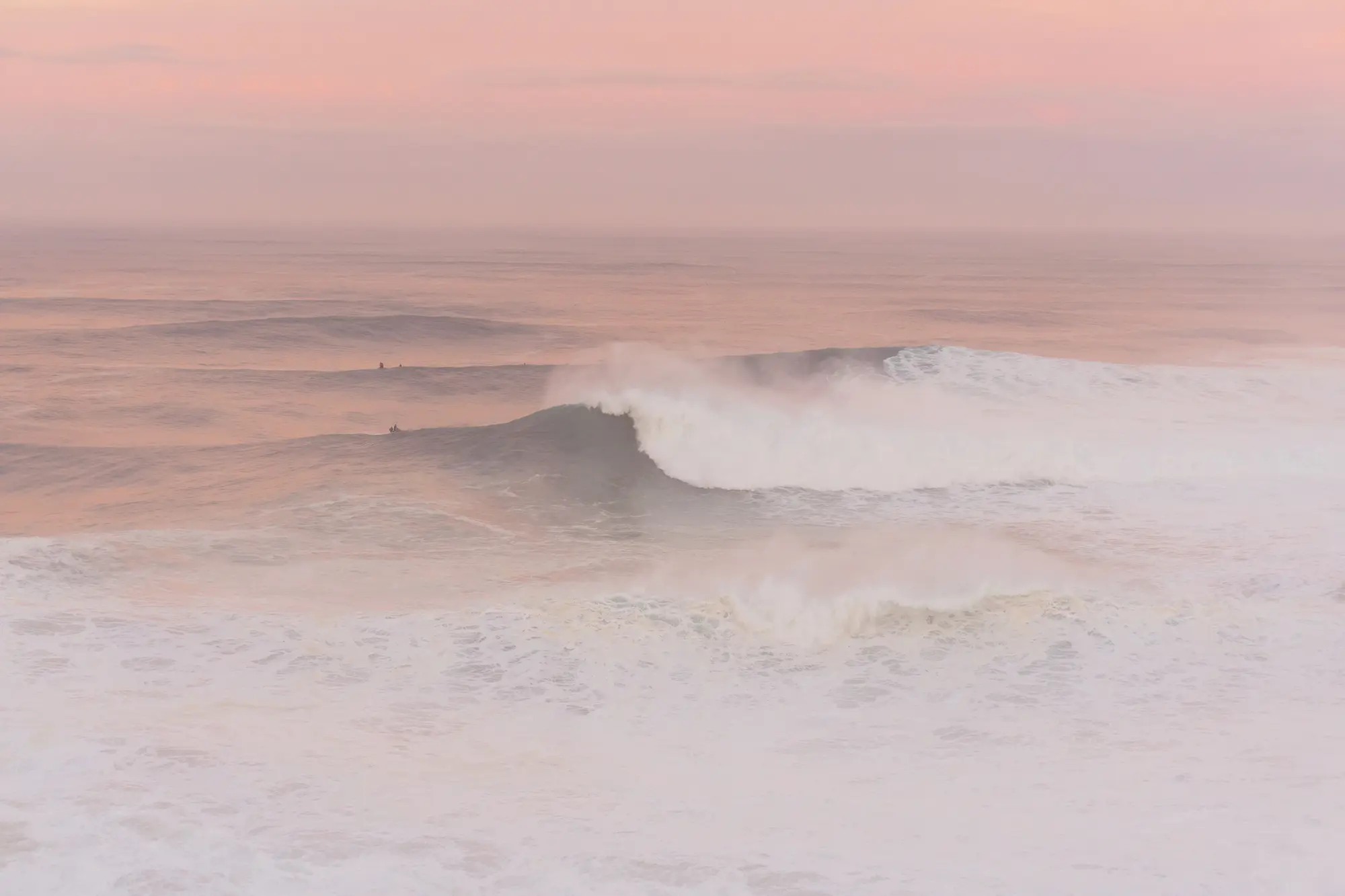 Pastel colored soft sunrise over the waves at Praia do Norte in Nazaré, Portugal.