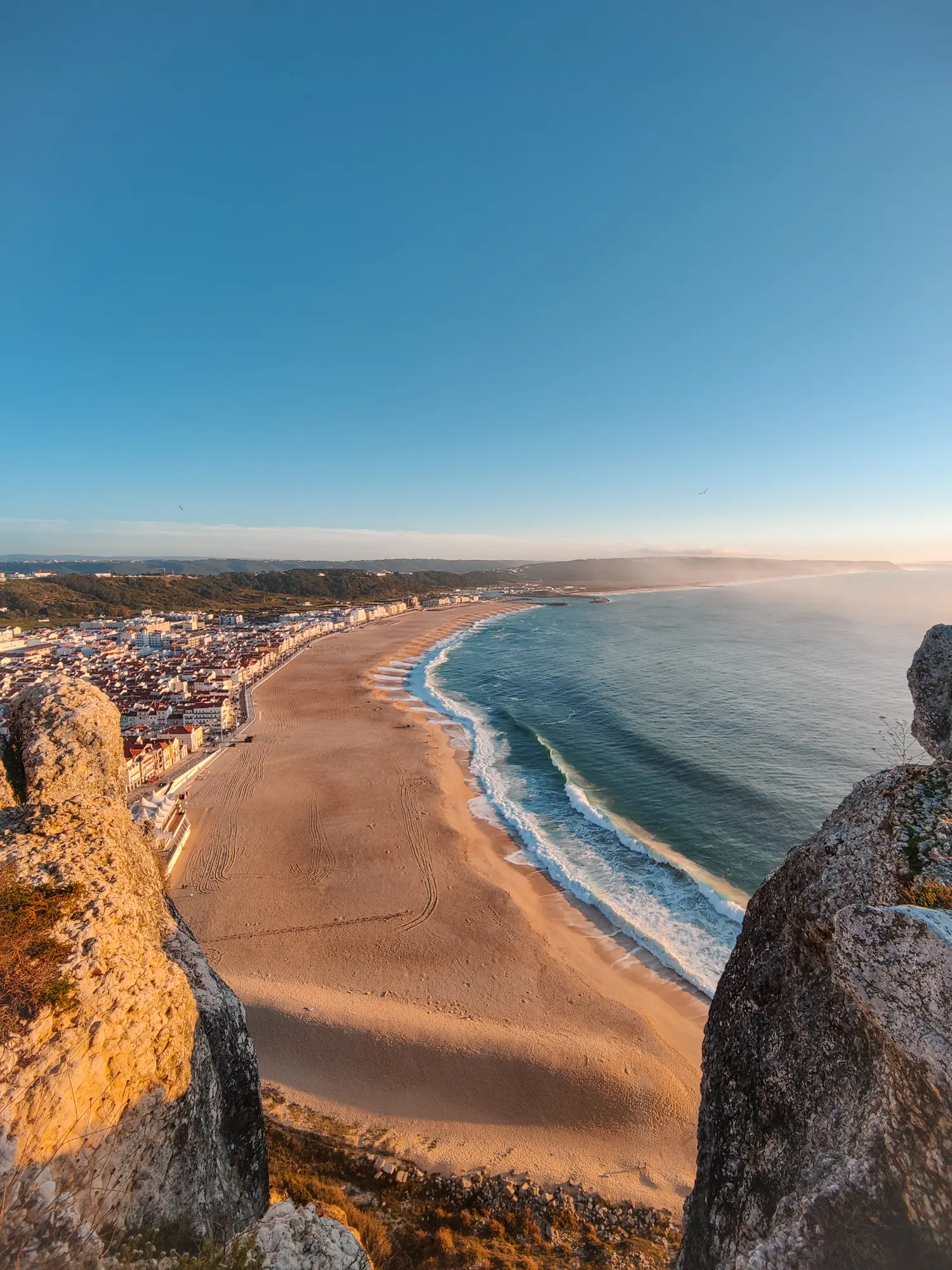 View from Nazaré viewpoint between two locks of Praia da Nazare, a long golden beach in Nazare, Portugal right before sunset.