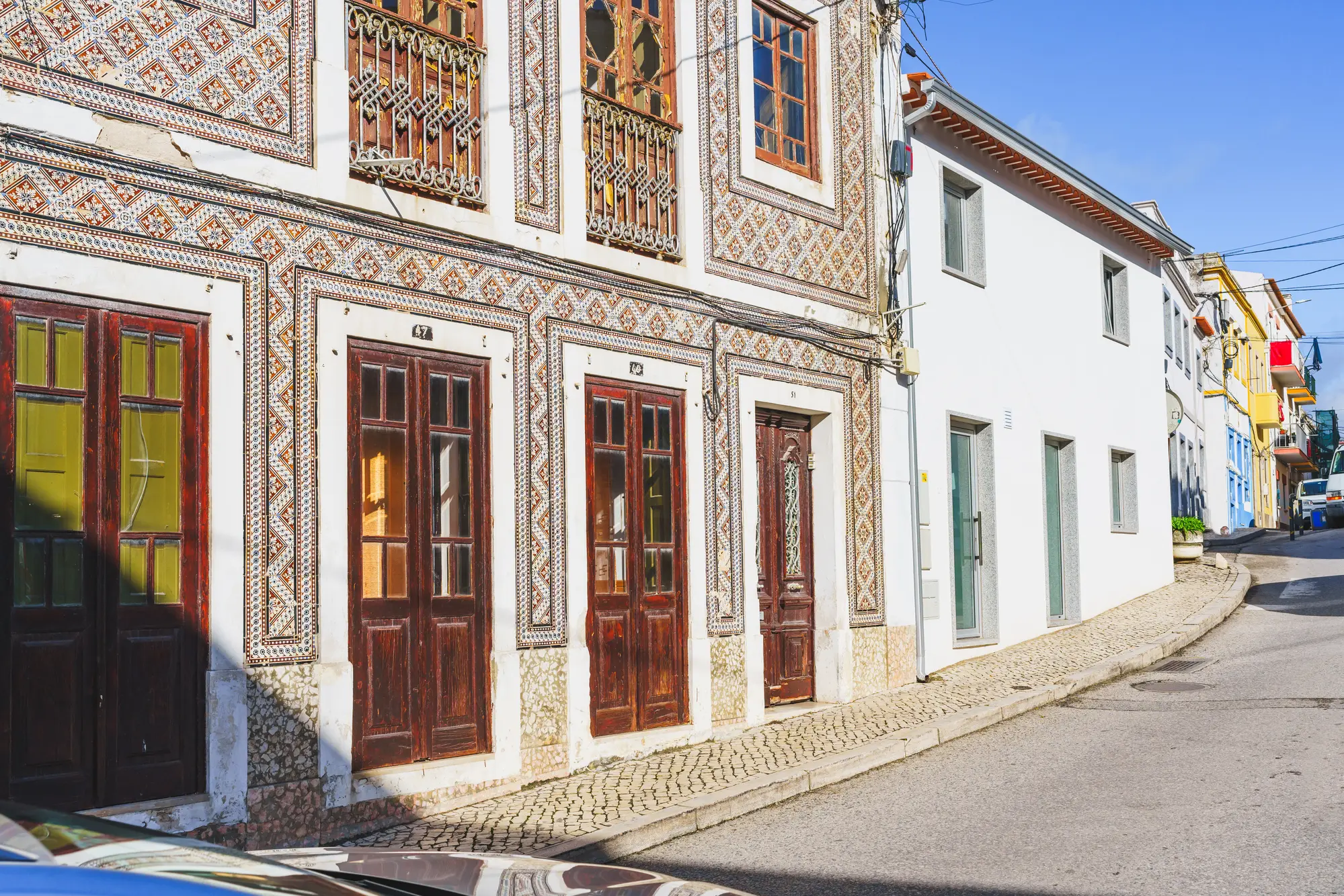 Traditional houses with brown wooden doors and azulejo tile along a street with cobbled sidewalks, in Sitio, one of the best places to stay in Nazare.