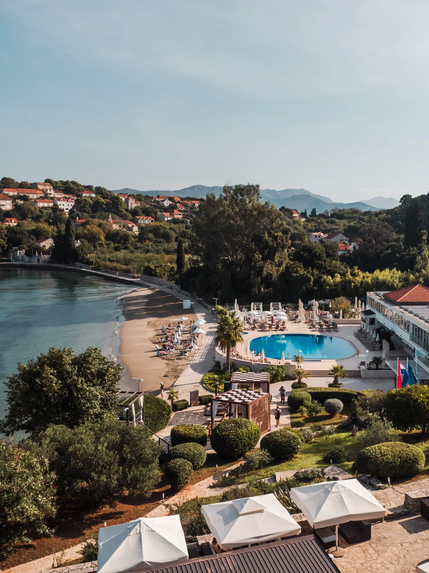 View of a round turquoise poos and orange rooftops of TUI BLUE resort on the beach surrounded by green trees on Kolocep Island, all-inclusive resort Dubrovnik.