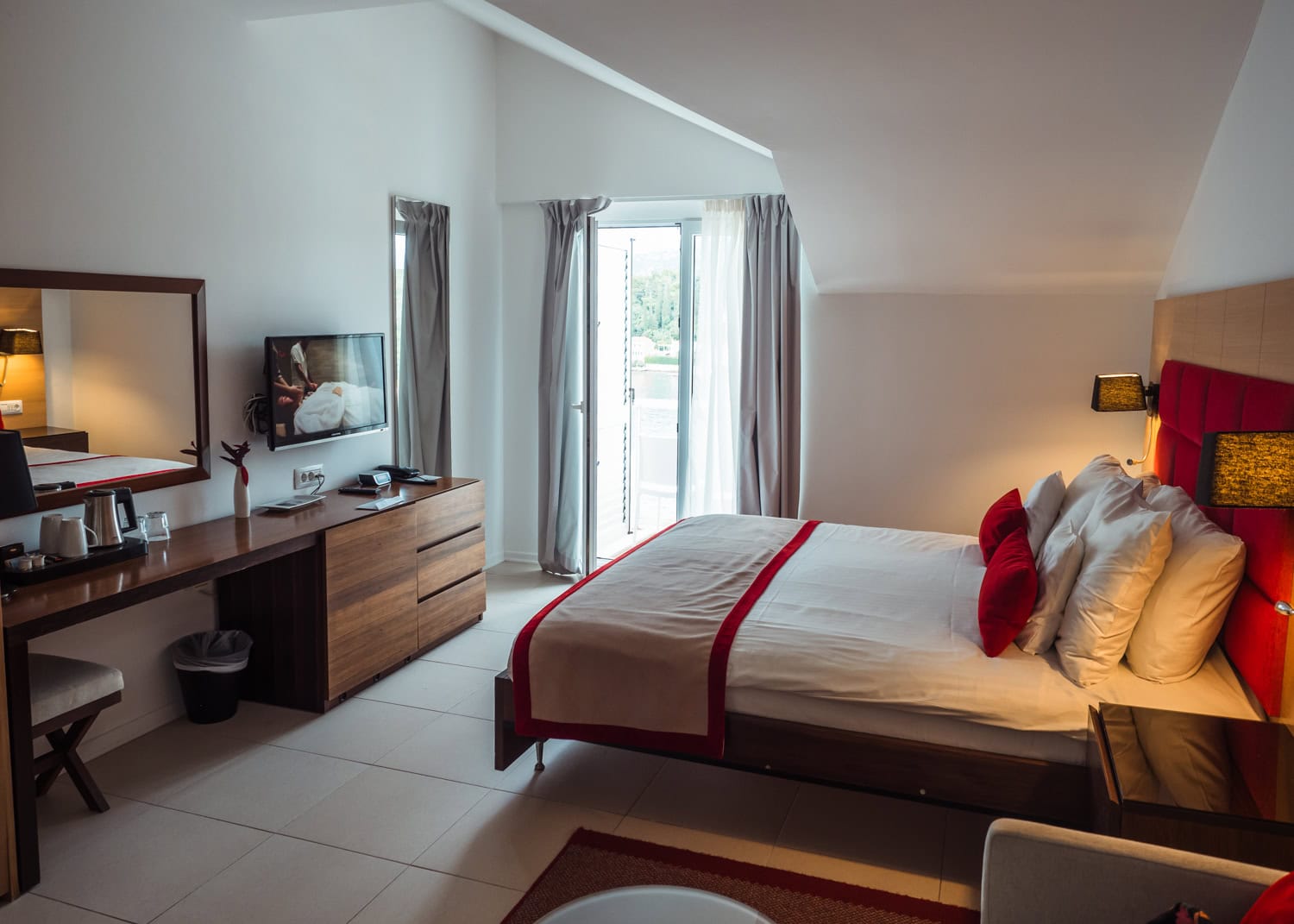White hotel room whit red accents, brown desk with tv, sun shining in from balcony doors at TUI BLUE Kalamota Island Resort Dubrovnik review.