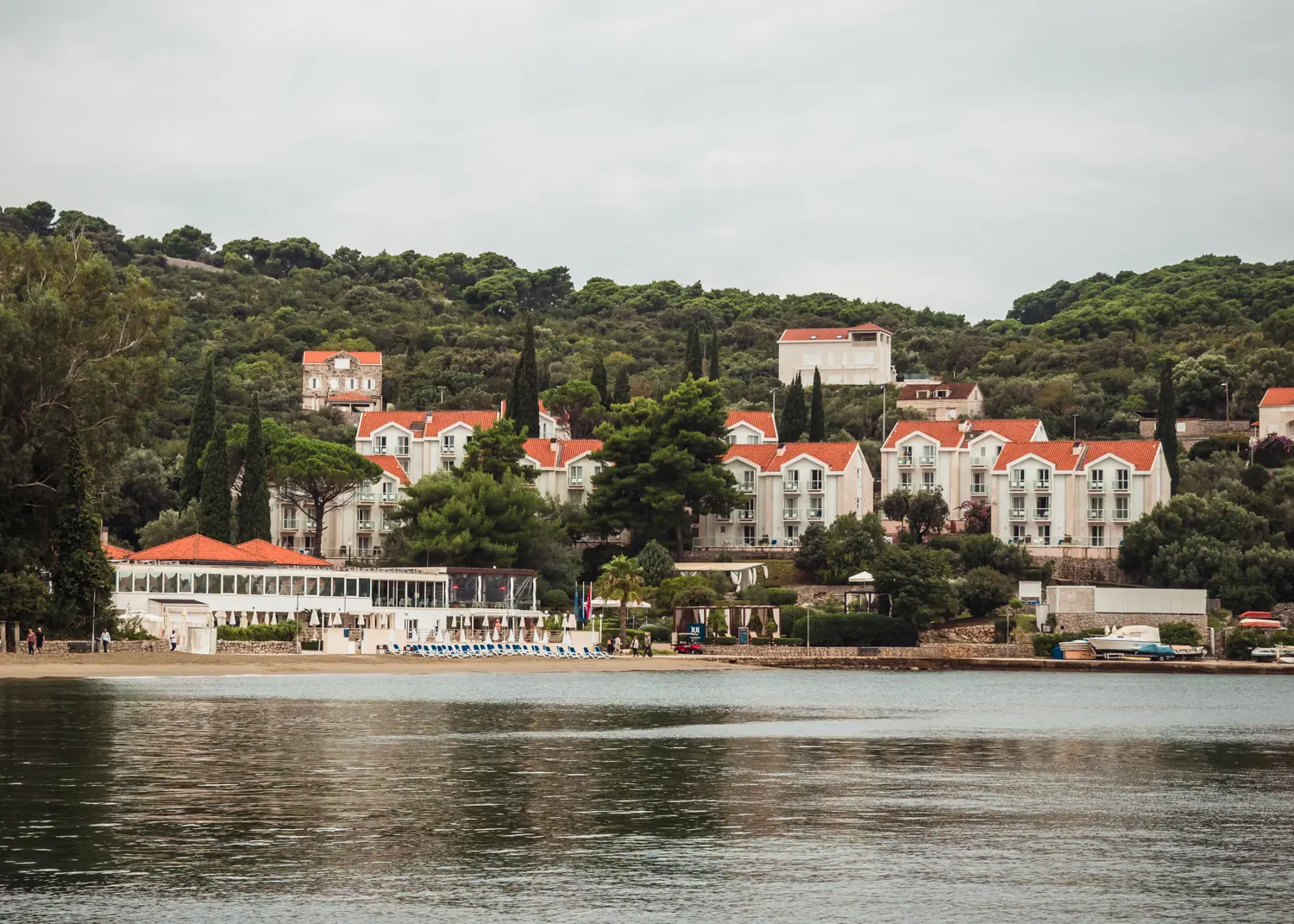 White buildings with orange roofs of TUI BLUE Kalamota Island Resort surrounded by greenery on the beach on a gloomy day in Kolocep Dubrovnik.