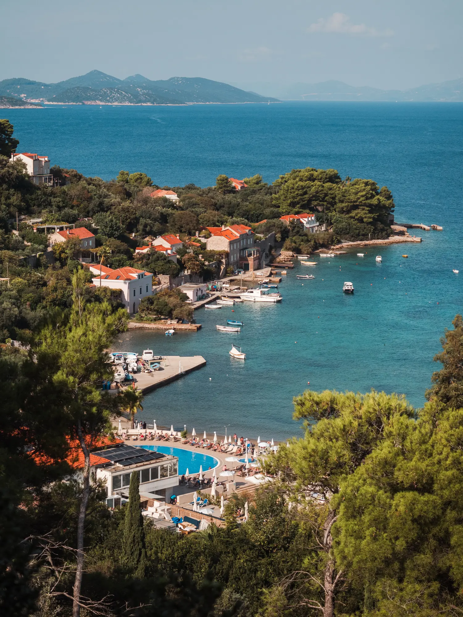 View from above of the turquoise pool and orange rooftops of TUI BLUE Kalamota Island Resort surrounded by green trees by the ocean on Koločep, Elaphiti Islands Dubrovnik.