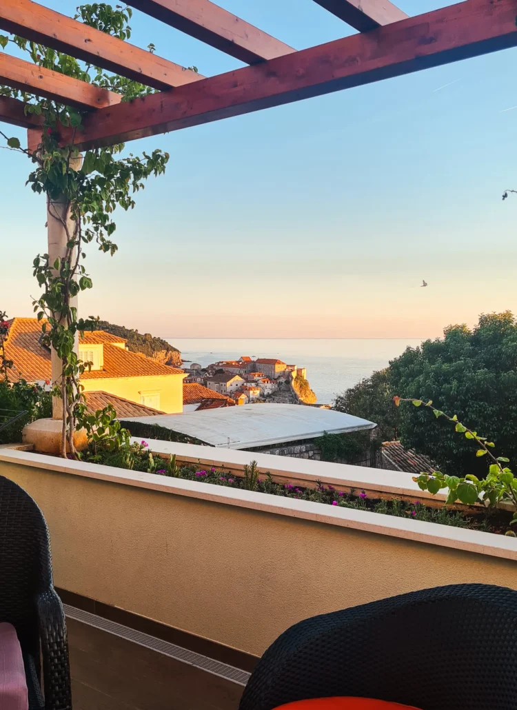 View from a balcony covered by a wooden pergola with green plants of Dubrovnik Old Town glowing in the sunset, one of the best apartments in Dubrovnik. Where to stay.