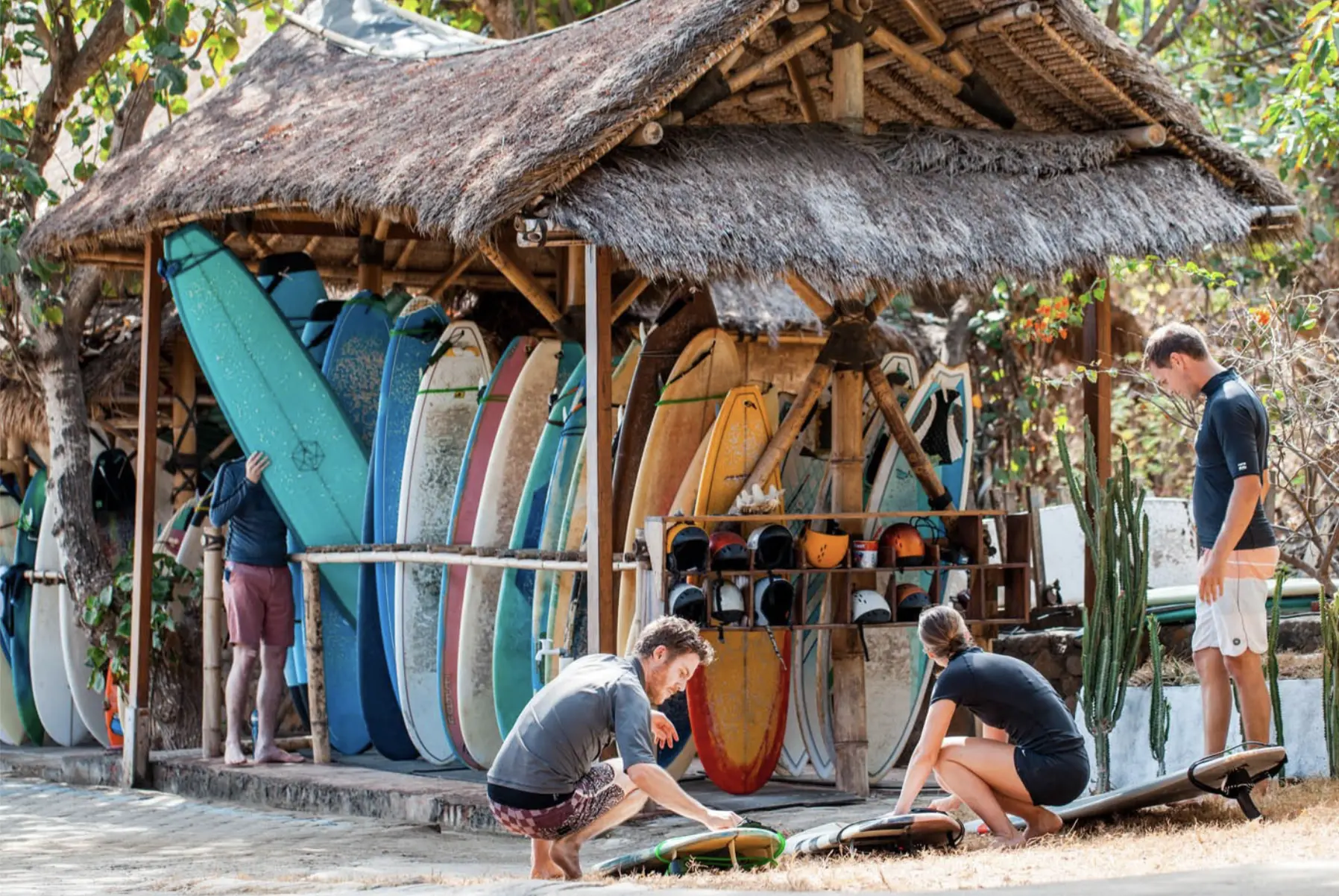 Four people choosing surfboards before a lesson from a straw hut full of colorful boards at the OG surf camp in Lombok.