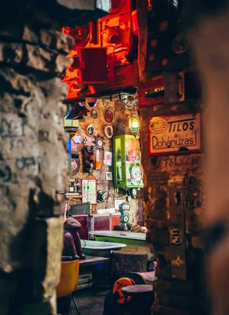 Looking through the stone entrance to one of the bars inside Szimpla Kert in Budapest. Bathtubs, green glass display cases on the stone walls, a metal hare, lots of little pictures and trinkets.