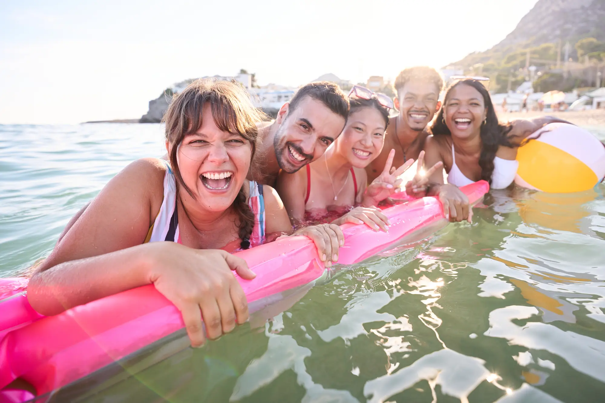 Three women and two men smiling to the camera while holding on the a pink floatie with the sun going down in the background while hosting a group trip to boost content creator income.